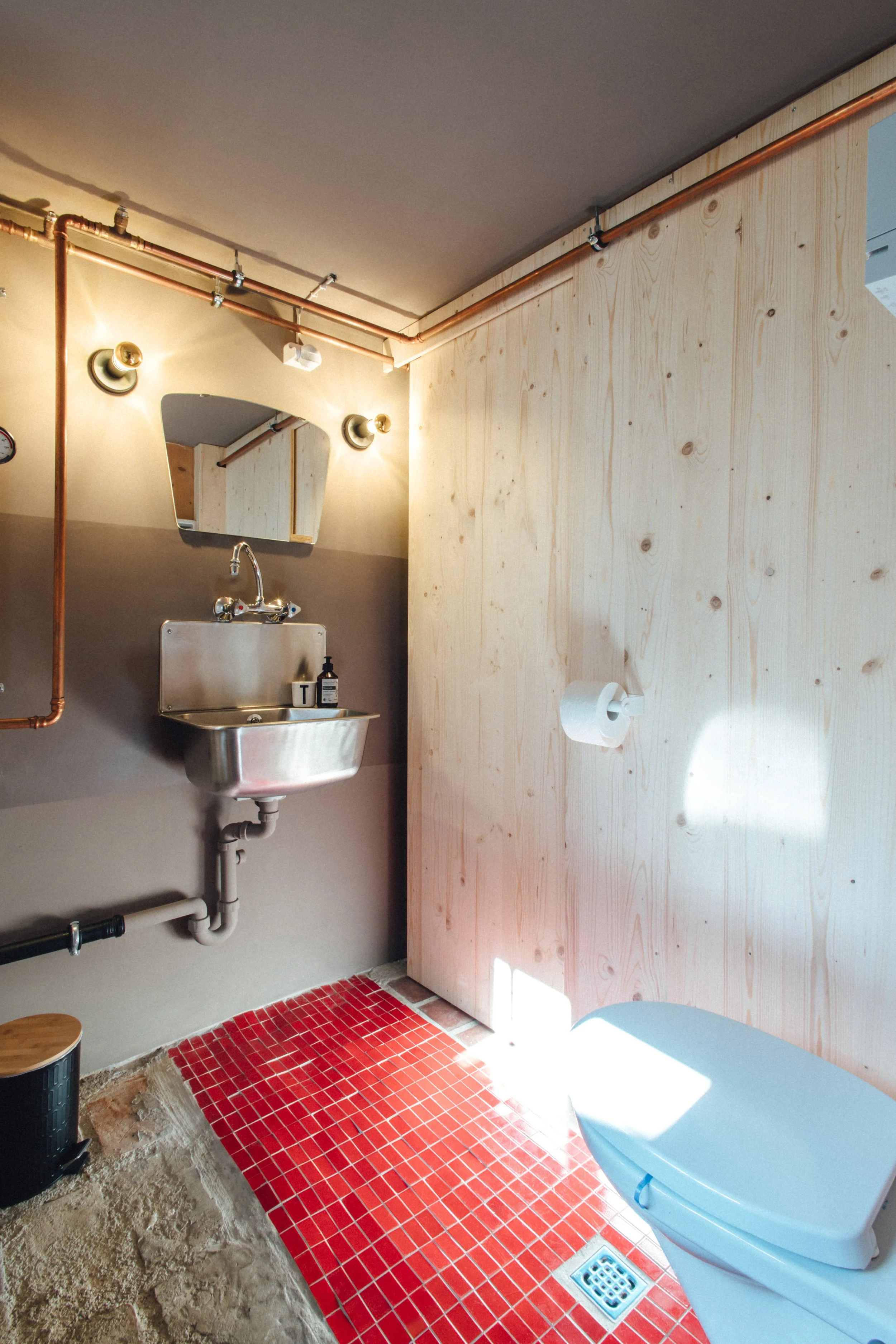 industrial Design Bad mit Kupferrohren und Retro Waschbecken, rustikale rote Bodenfliesen