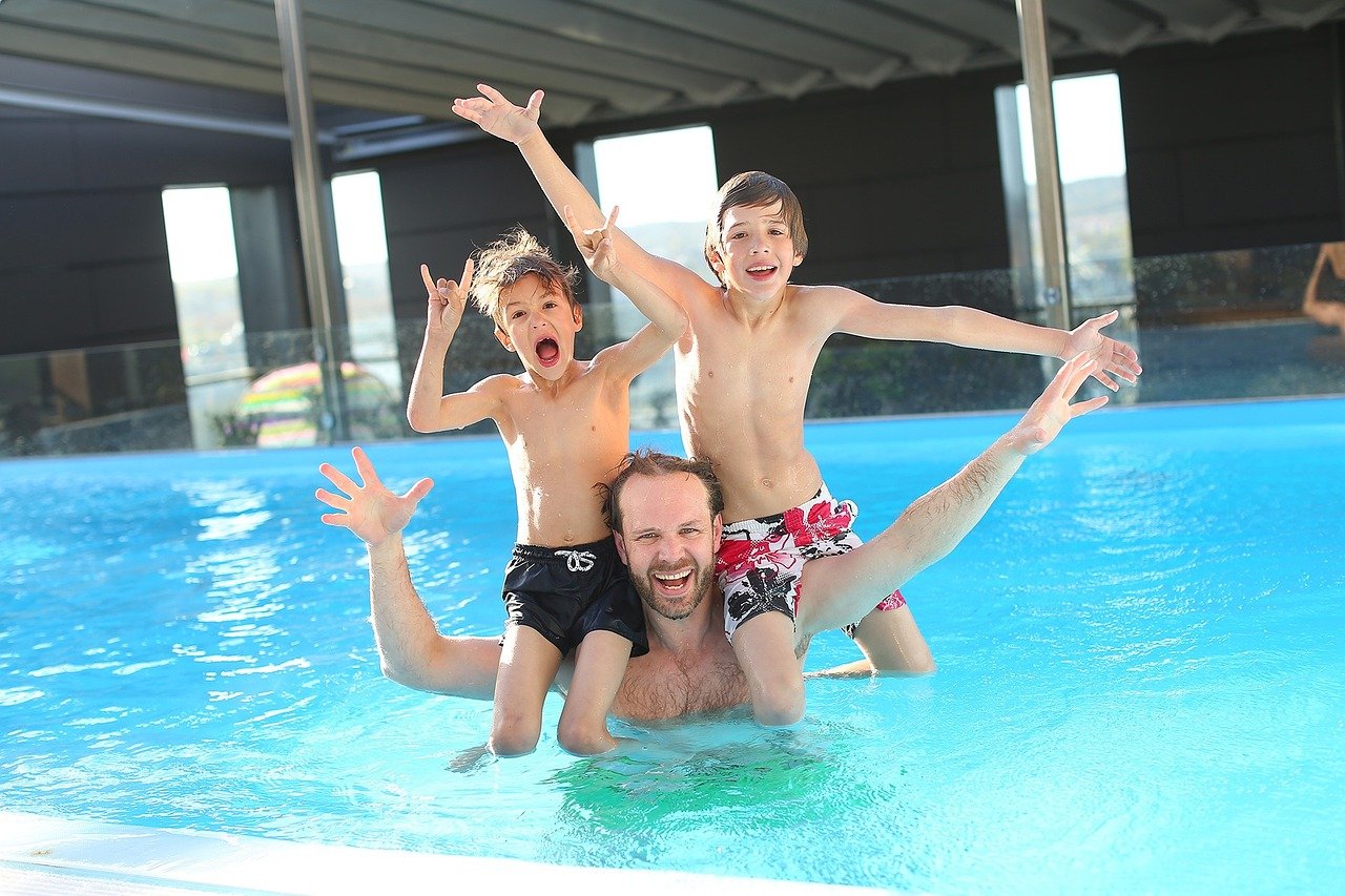 Man with two children playing in a swimming pool, laughing and having fun