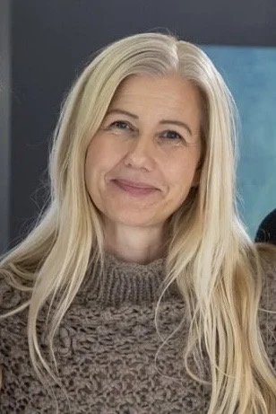 Person med langt blondt hår, iført en strikket genser, smiler mot kameraet.