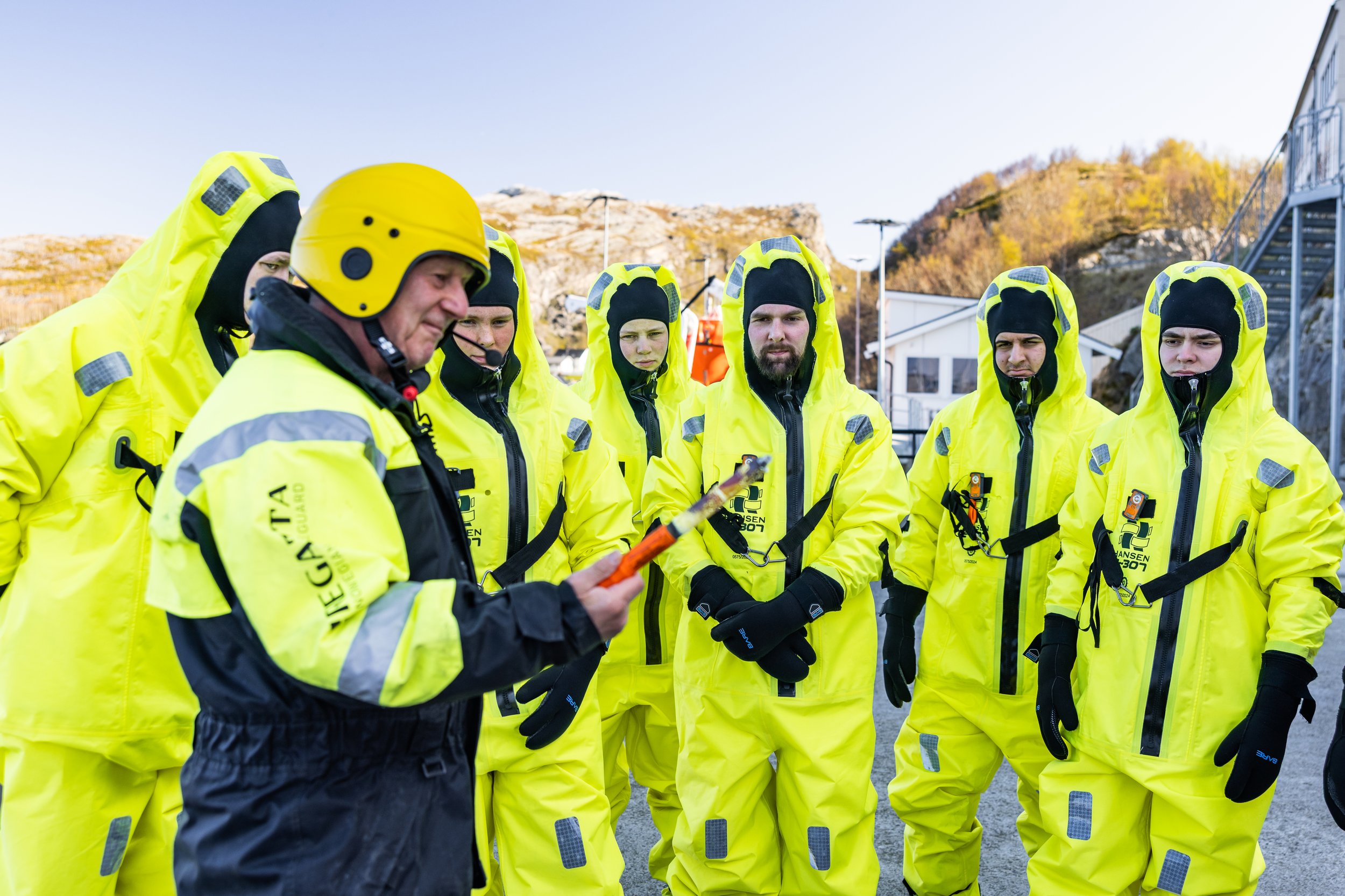 En gruppe personer i gule redningsdrakter står sammen utendørs mens en person holder et bluss.