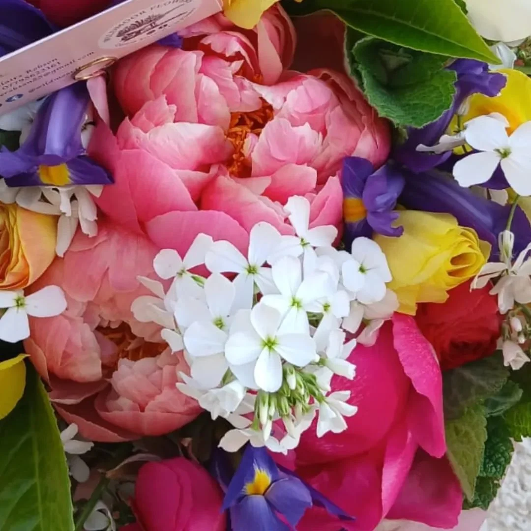 Colorful bouquet of pink peonies, white phlox, yellow roses, purple irises, and green leaves.
