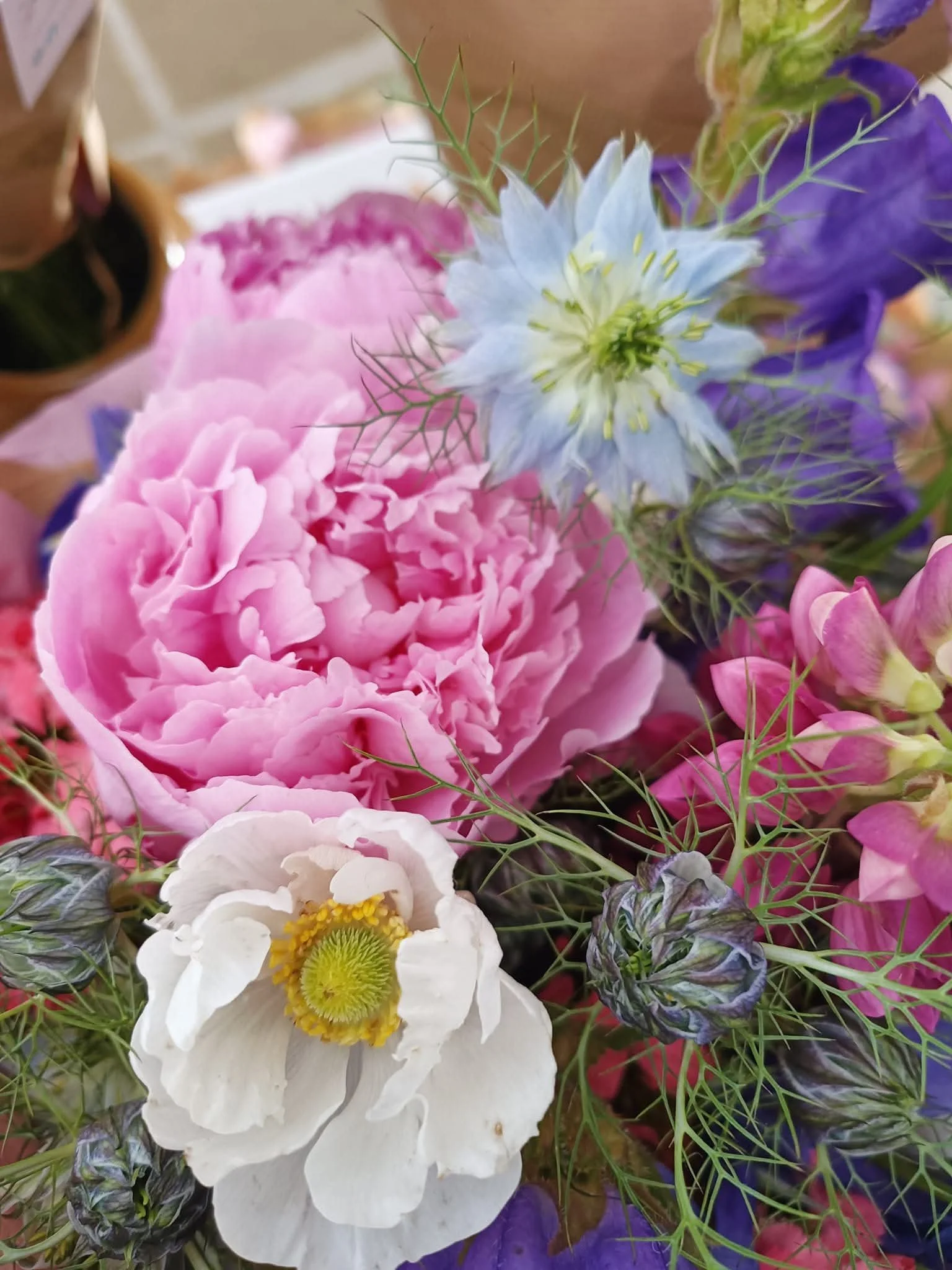 Close-up of a bouquet of flowers with pink peony, blue and purple flowers, a white poppy, and greenery.