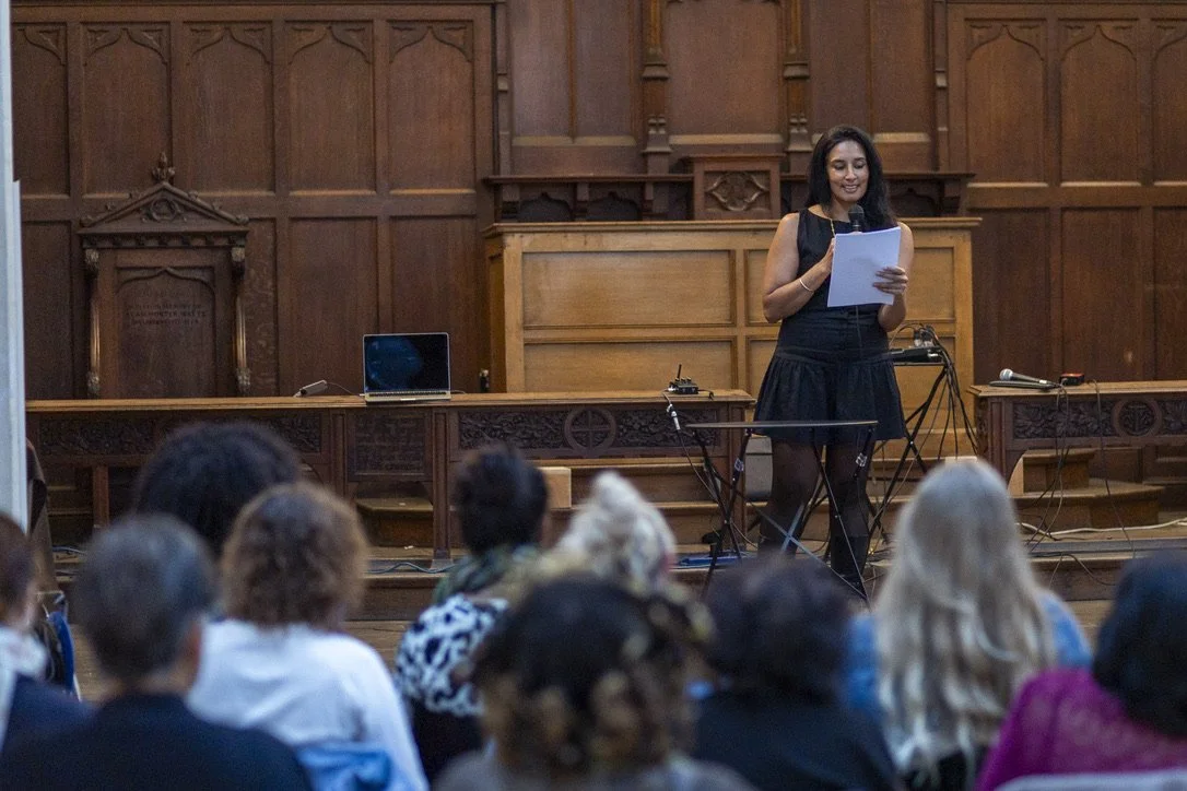 Woman giving a presentation to an audience in a wood-paneled room.