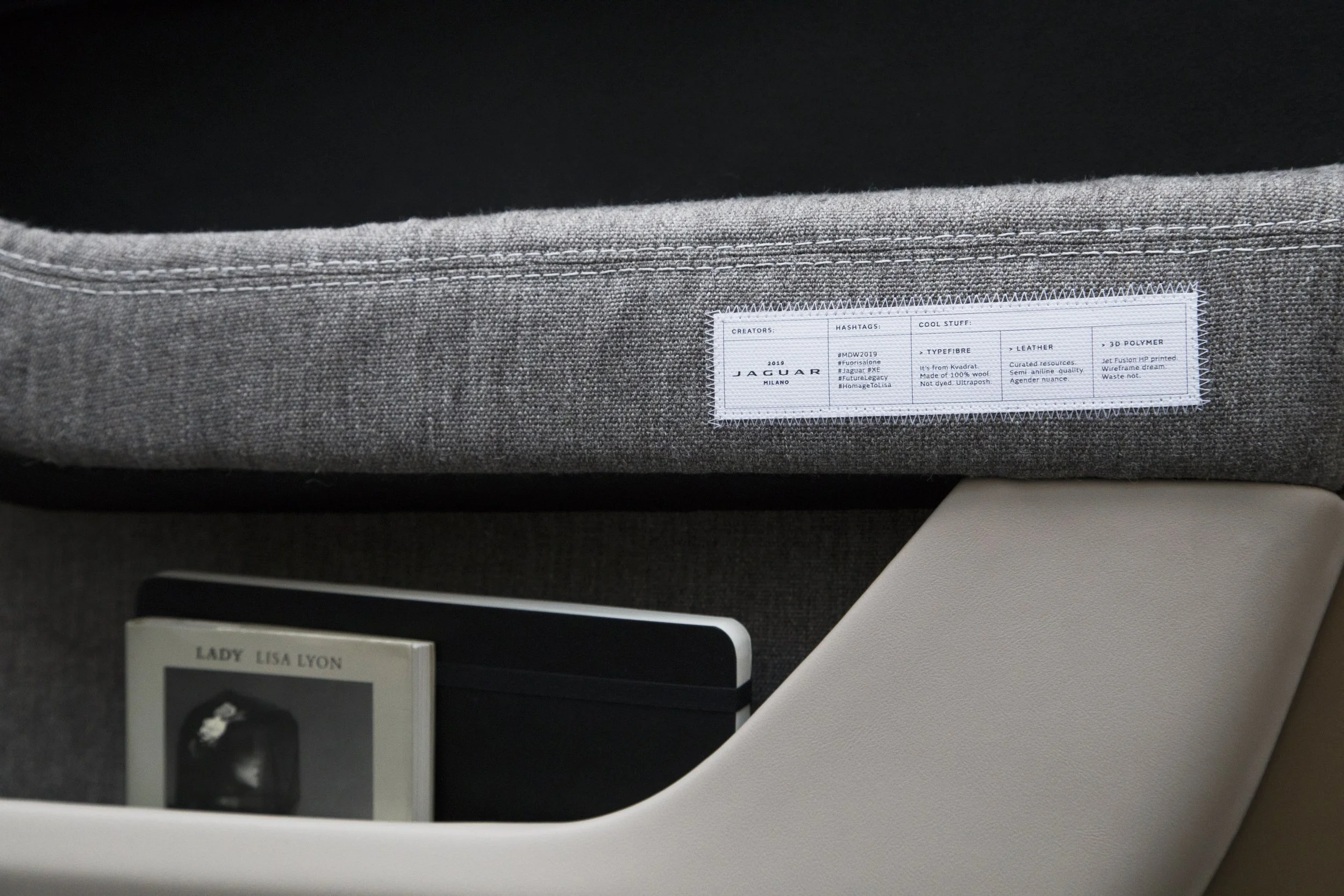 Close-up of a car interior door pocket with fabric label from Jaguar design project, holding a book titled 'Lady Lisa Lyon' and a notebook.