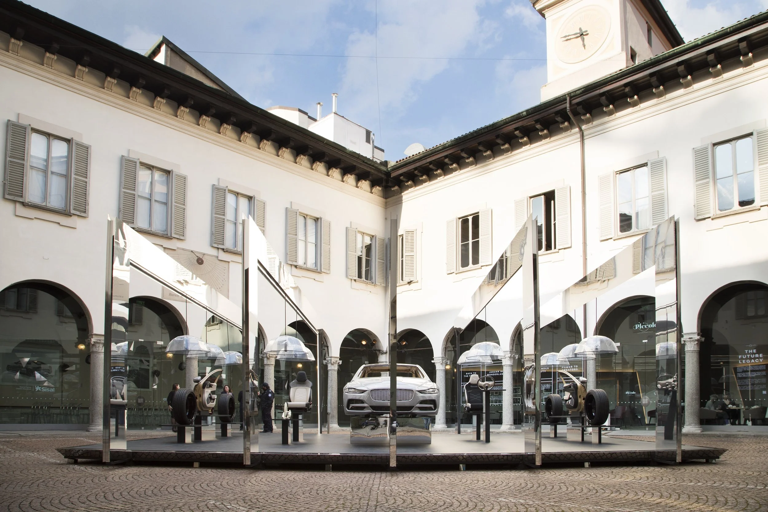 Car display in a courtyard with mirrors reflecting a white building