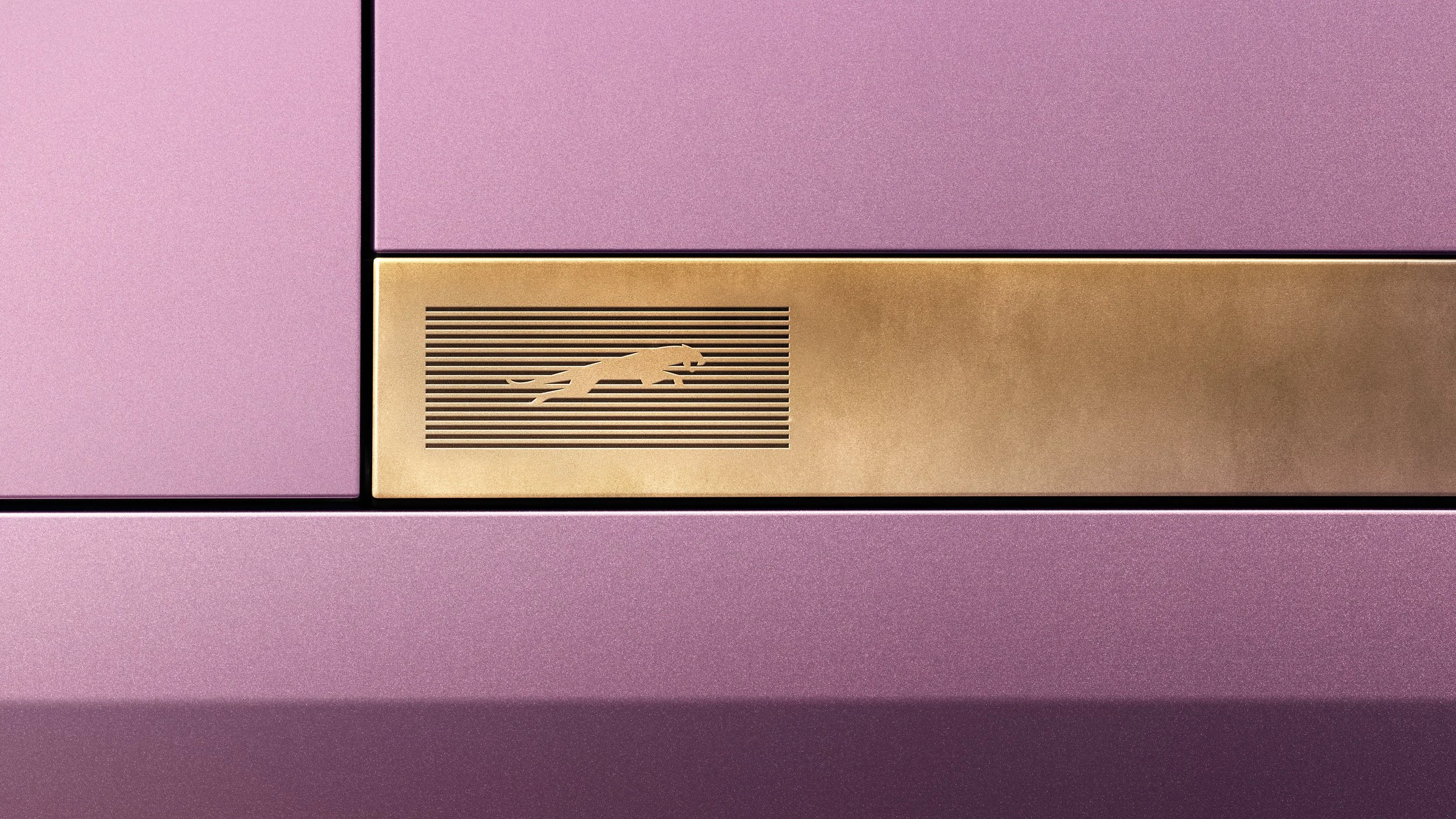 Close-up of a pink metallic surface with a gold panel featuring a stylized panther logo and horizontal lines.