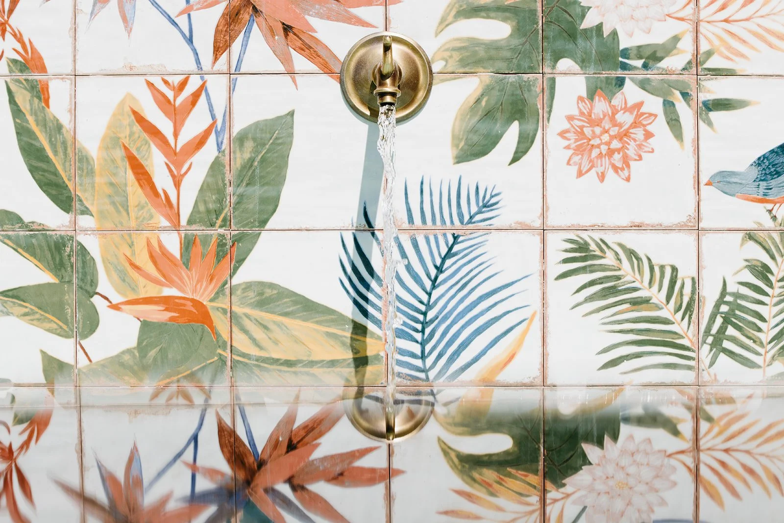 Brass wall fountain flowing over colorful tropical floral tiles