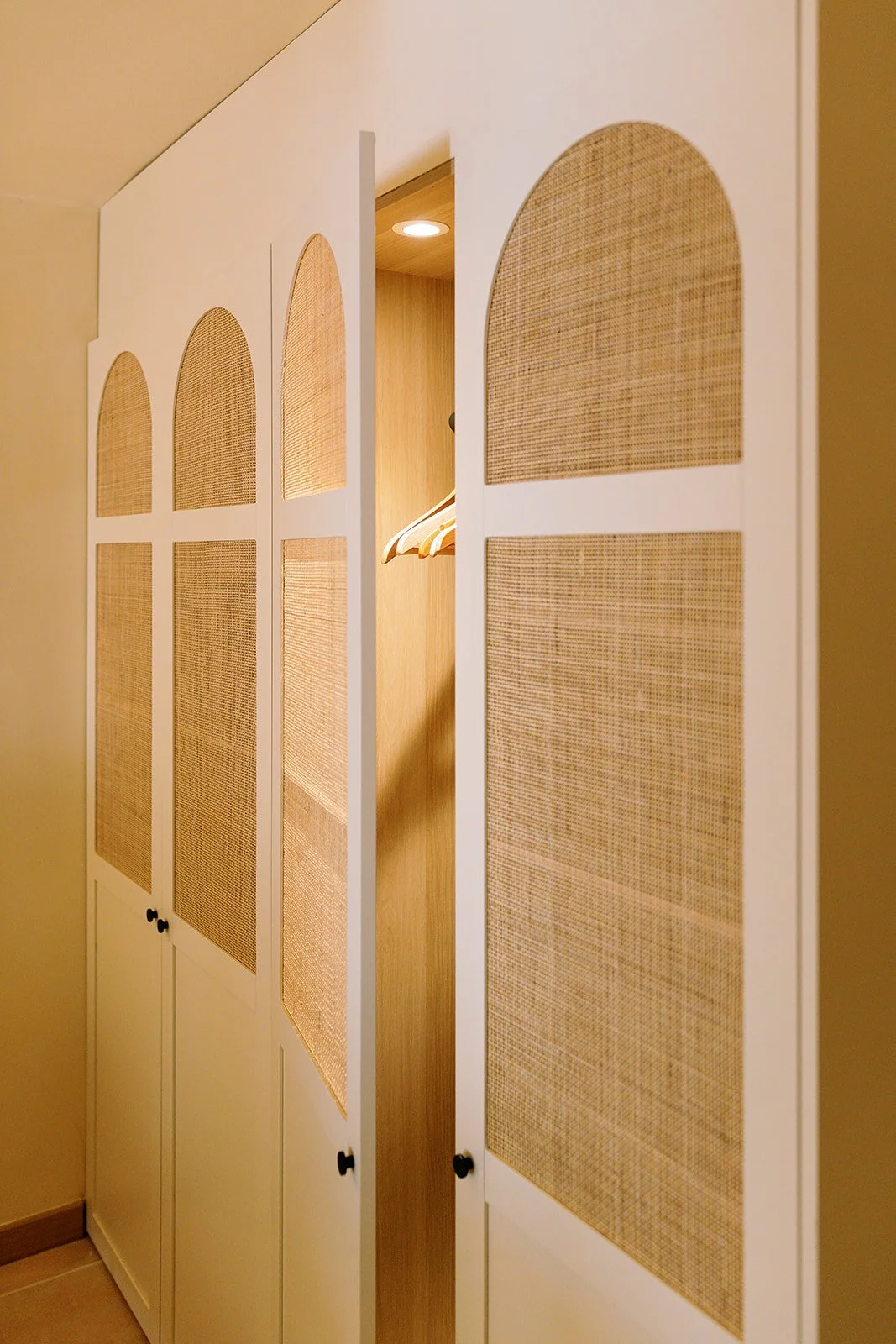 White built-in closet doors with woven rattan panels, arched detailing, and warm wood interior