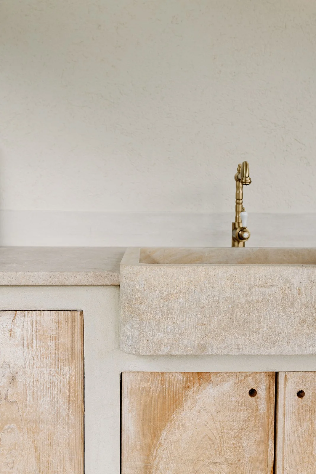 Close-up of a rustic stone farmhouse sink with a vintage brass faucet and unfinished wood cabinetry.