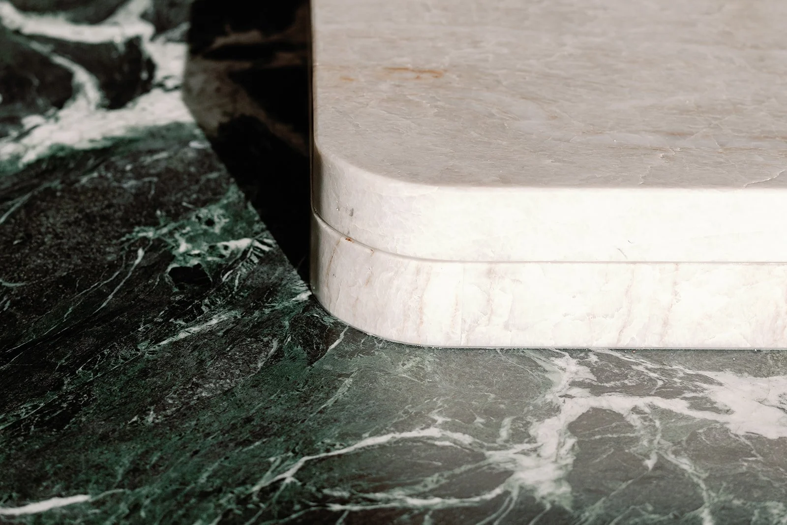 Close-up of a white cylindrical marble pedestal on a dark green marble floor