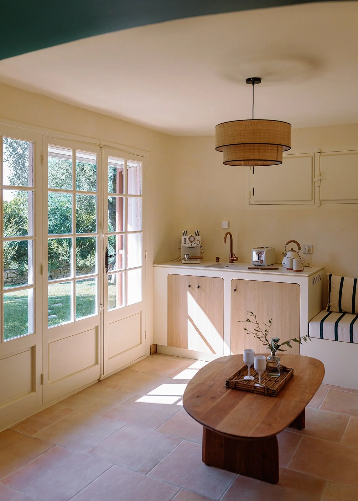 Bright rustic kitchen with a woven pendant light, French doors, wood dining table, coffee maker, toaster, kettle, and built-in bench seating