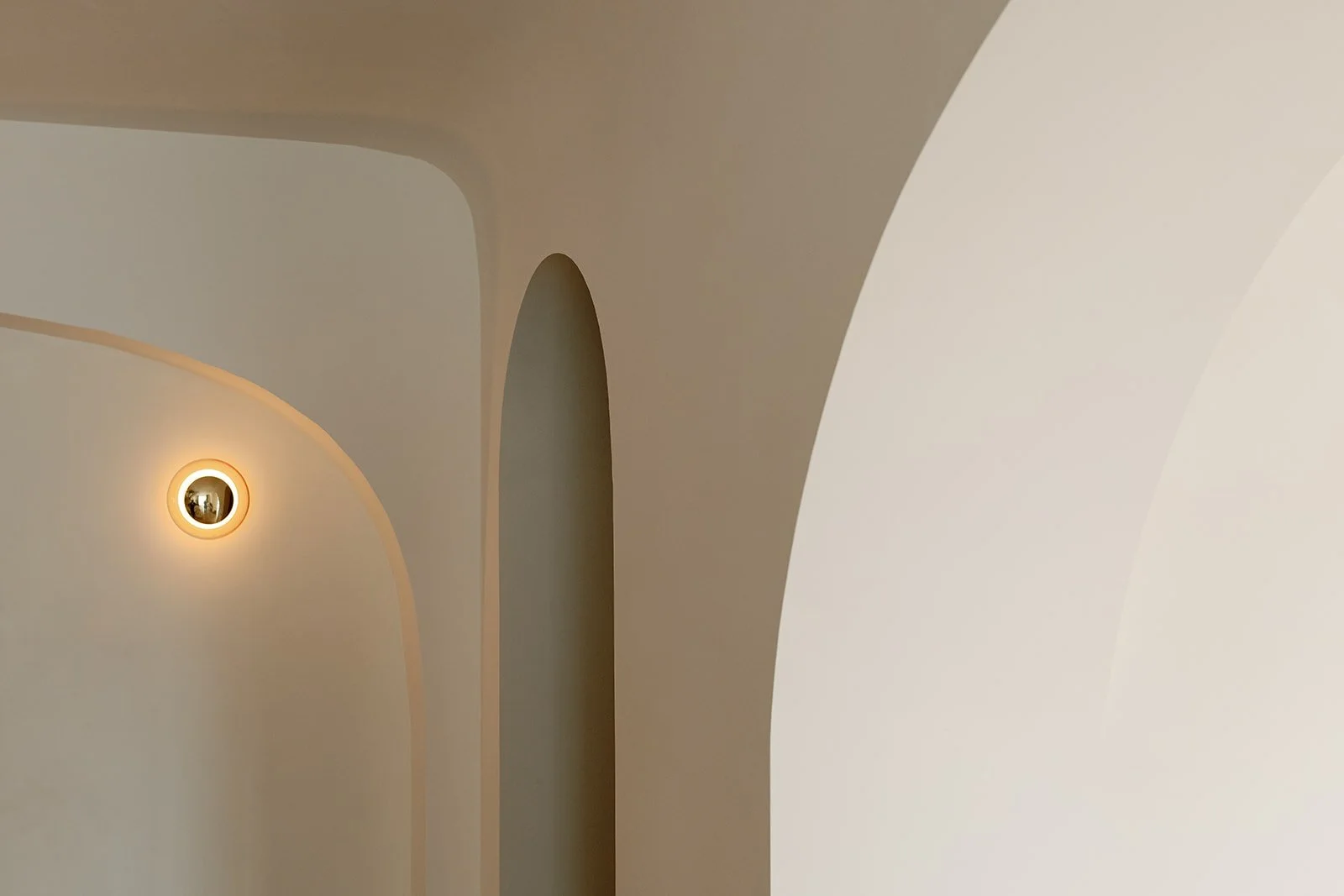 Minimalist beige interior with curved architectural archways and a glowing recessed wall light