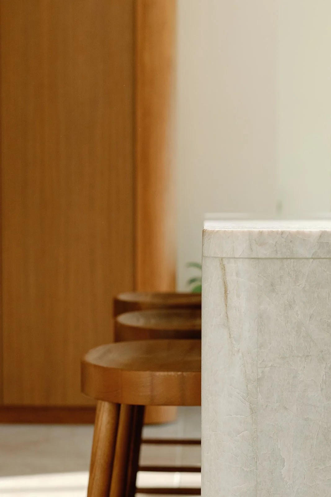 Minimalist interior with wooden stools, a white textured counter, and warm wood-paneled walls