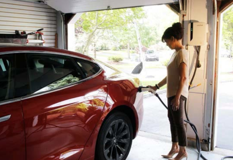 A woman plugging in a red electric car in a garage.