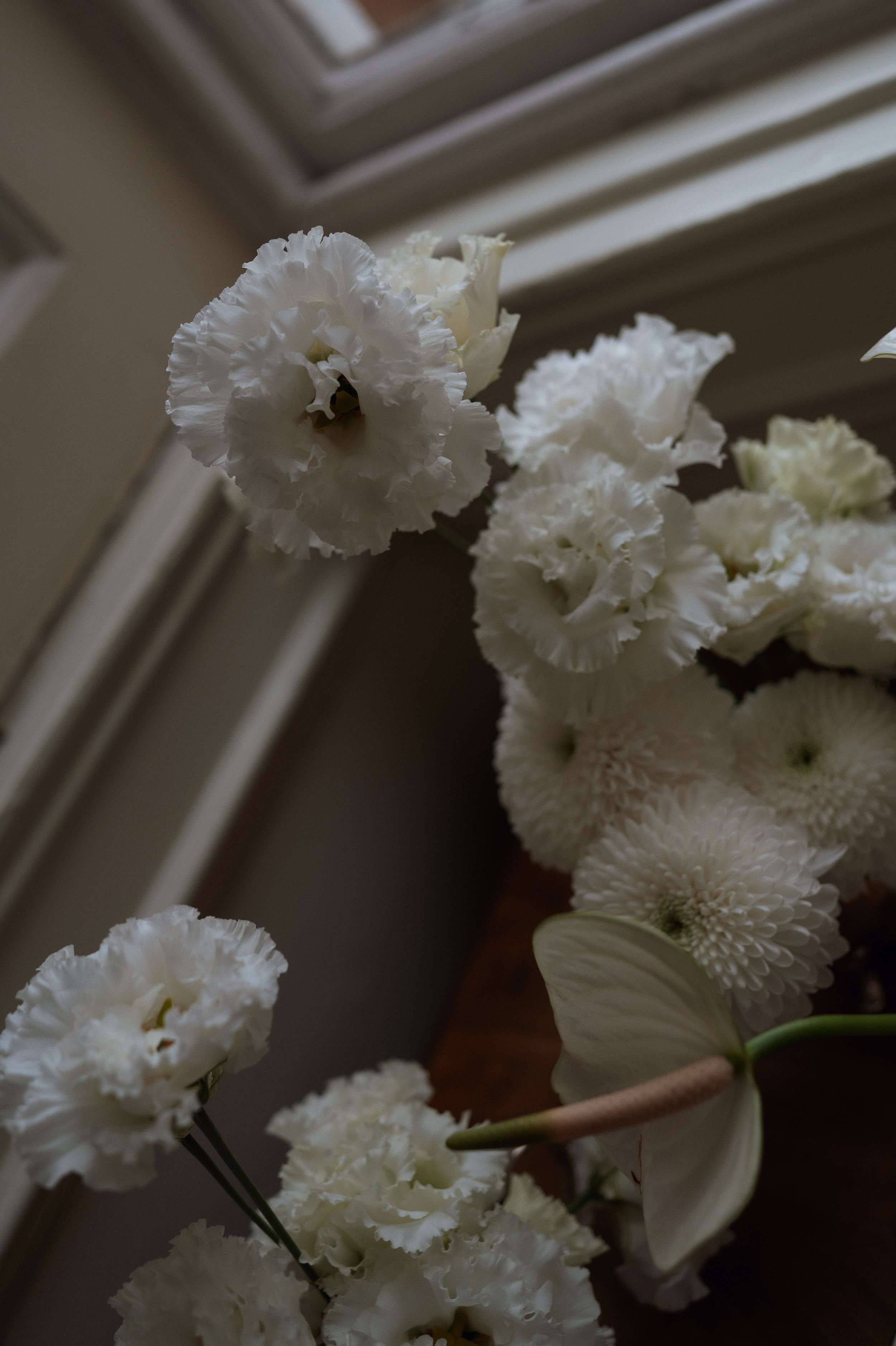 White flowers, including lisianthus, as part of a floral arrangement placed on a wooden surface near a window.