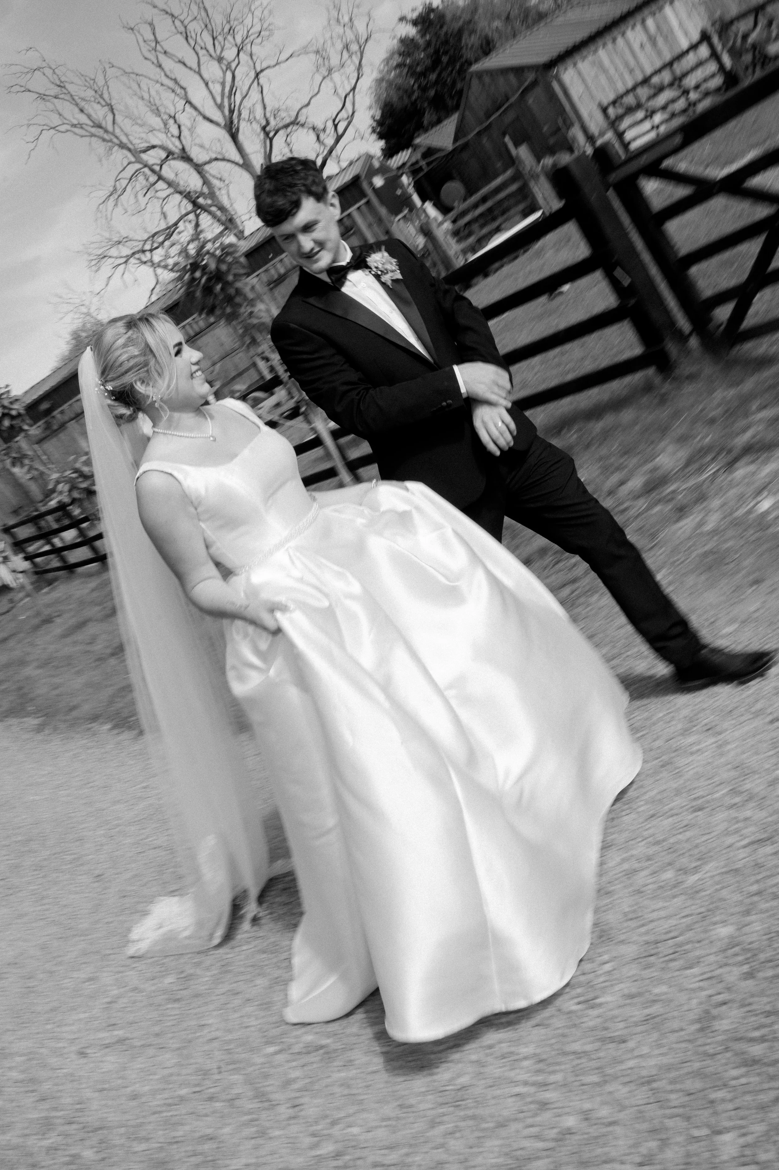 Black and white photo of a bride and groom walking outside, smiling at each other during a wedding.