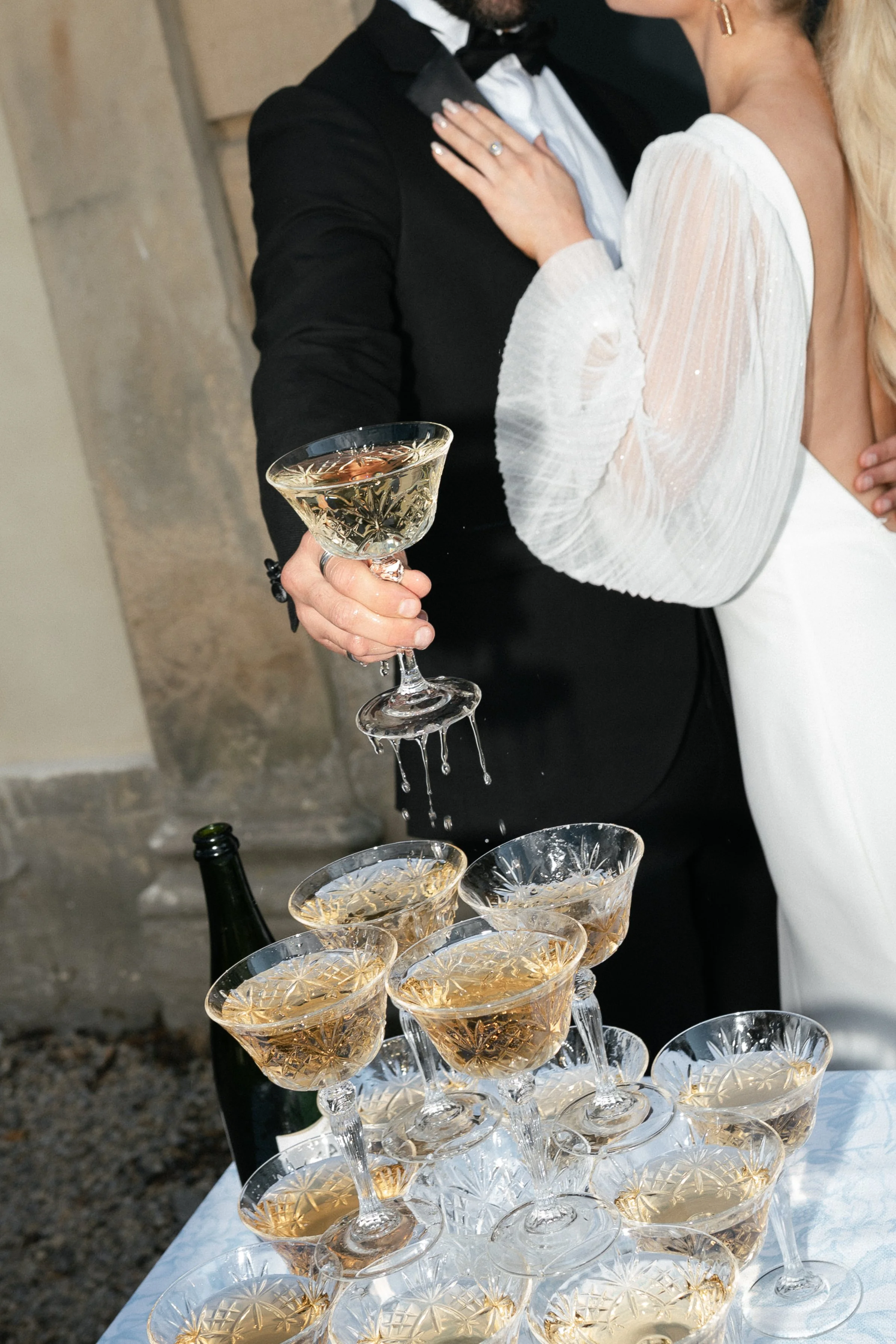 A bride and groom celebrating, with the groom pouring champagne into a pyramid of glasses.