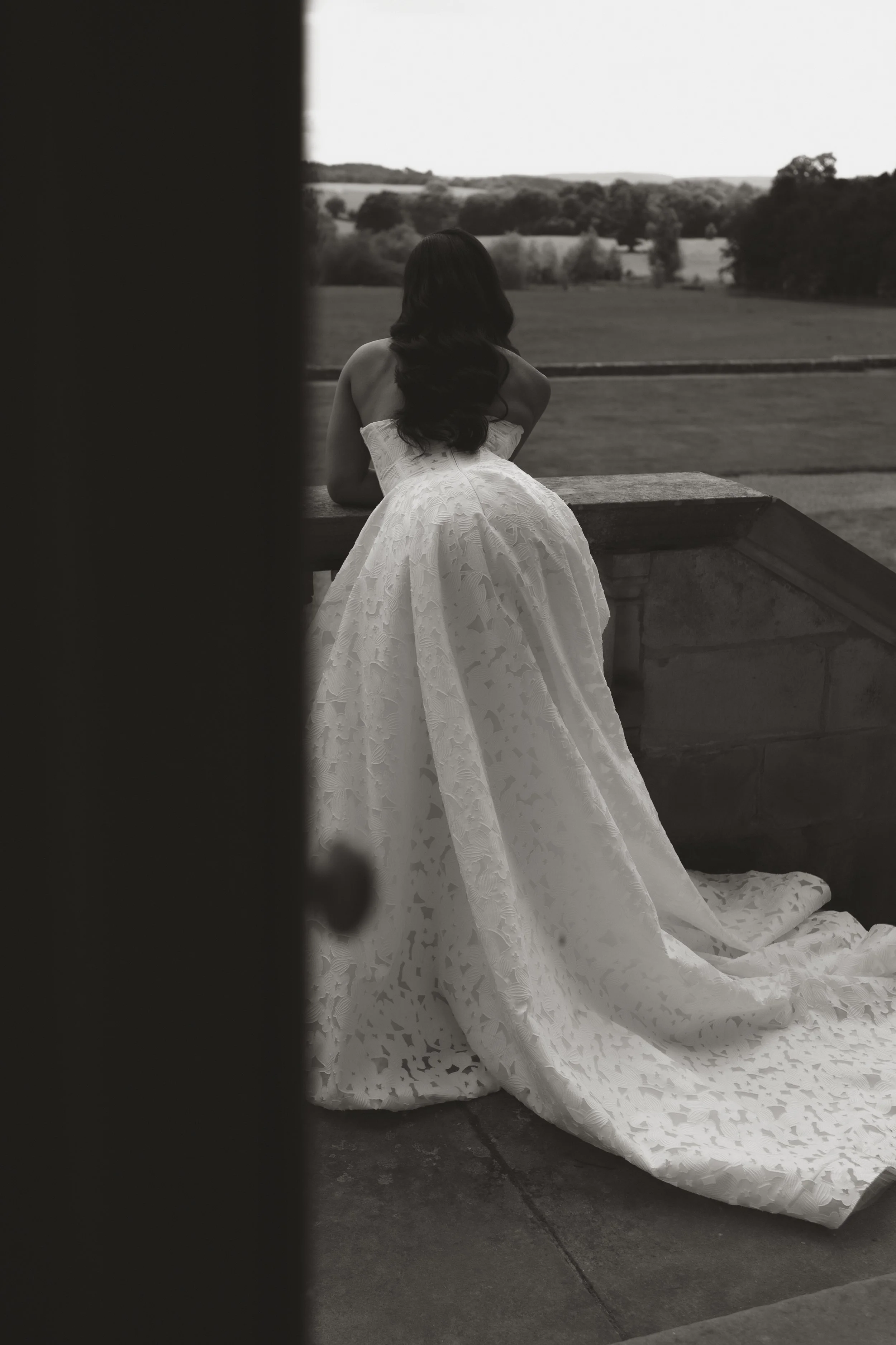 A woman in a wedding dress standing on a porch, looking out over a rural landscape.