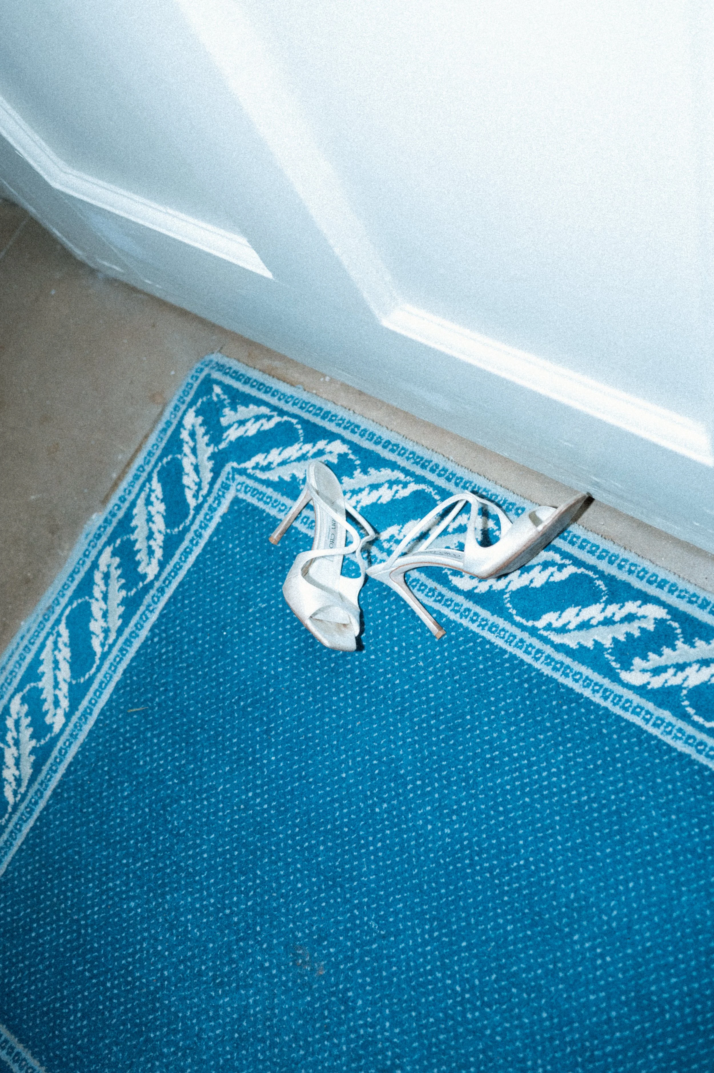 A pair of white high-heeled shoes on a blue patterned rug near a white door.