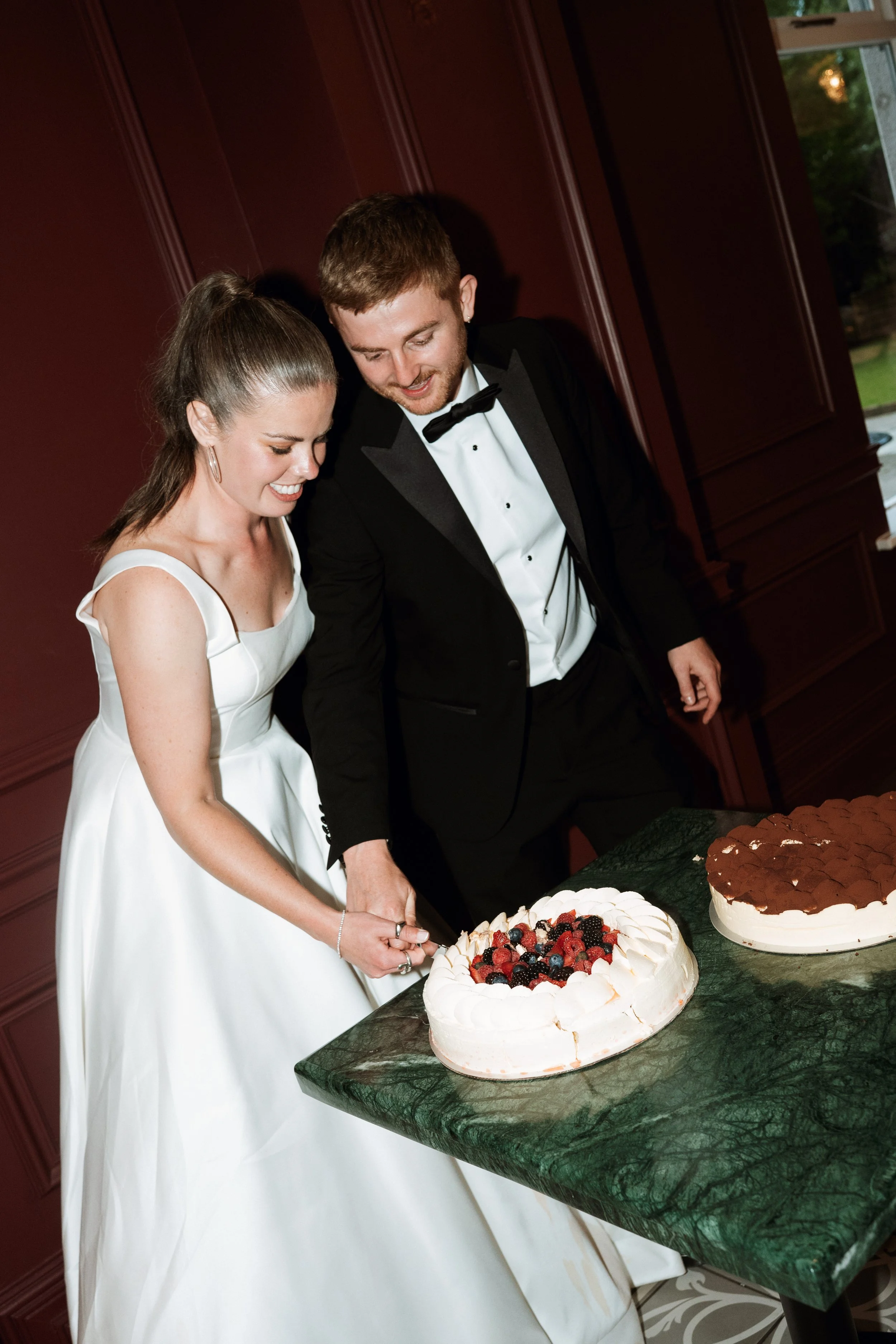 A bride and groom in wedding attire cutting a wedding cake together at a reception.