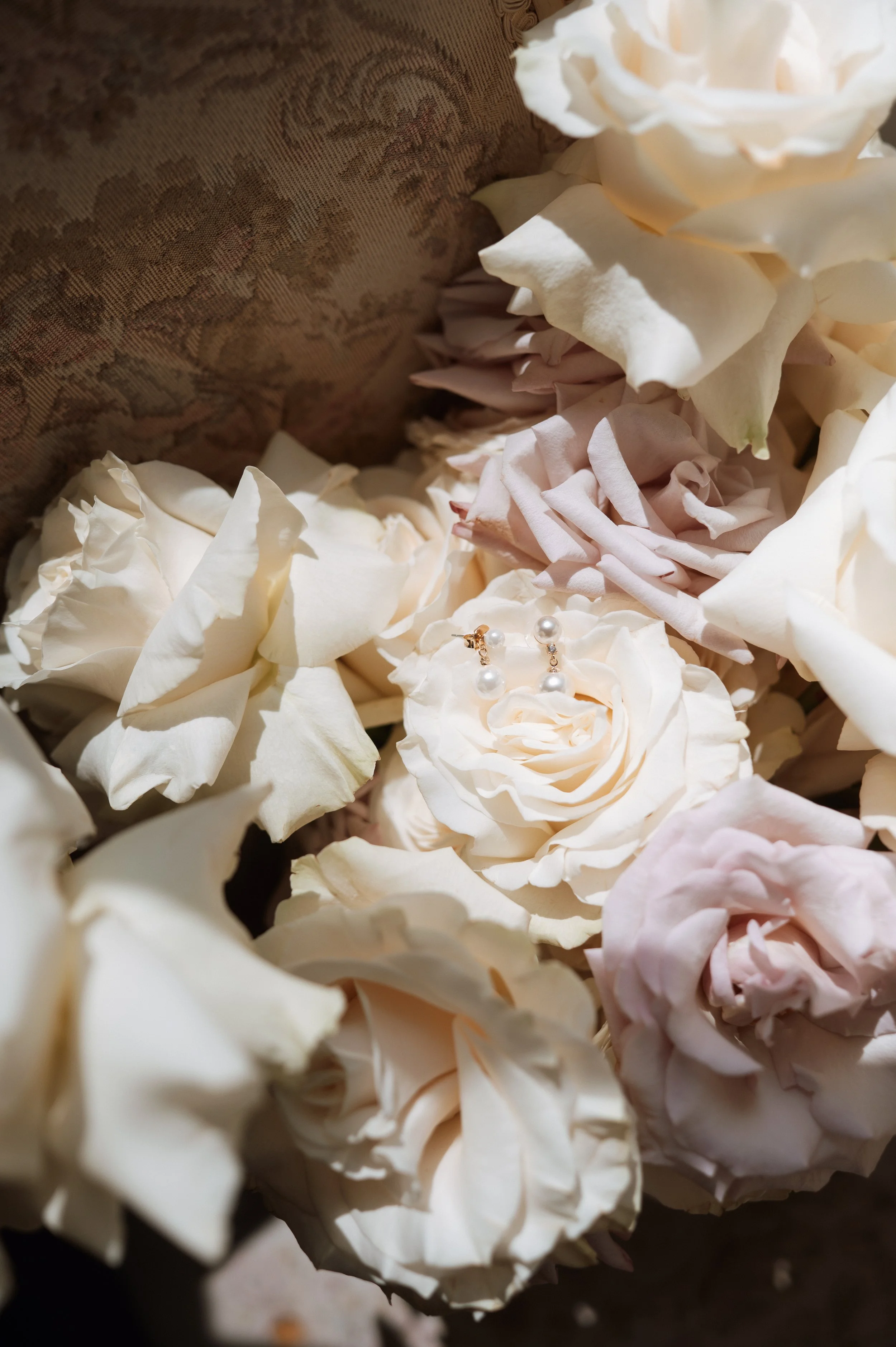 White and light pink roses with pearl earrings placed among the flowers.
