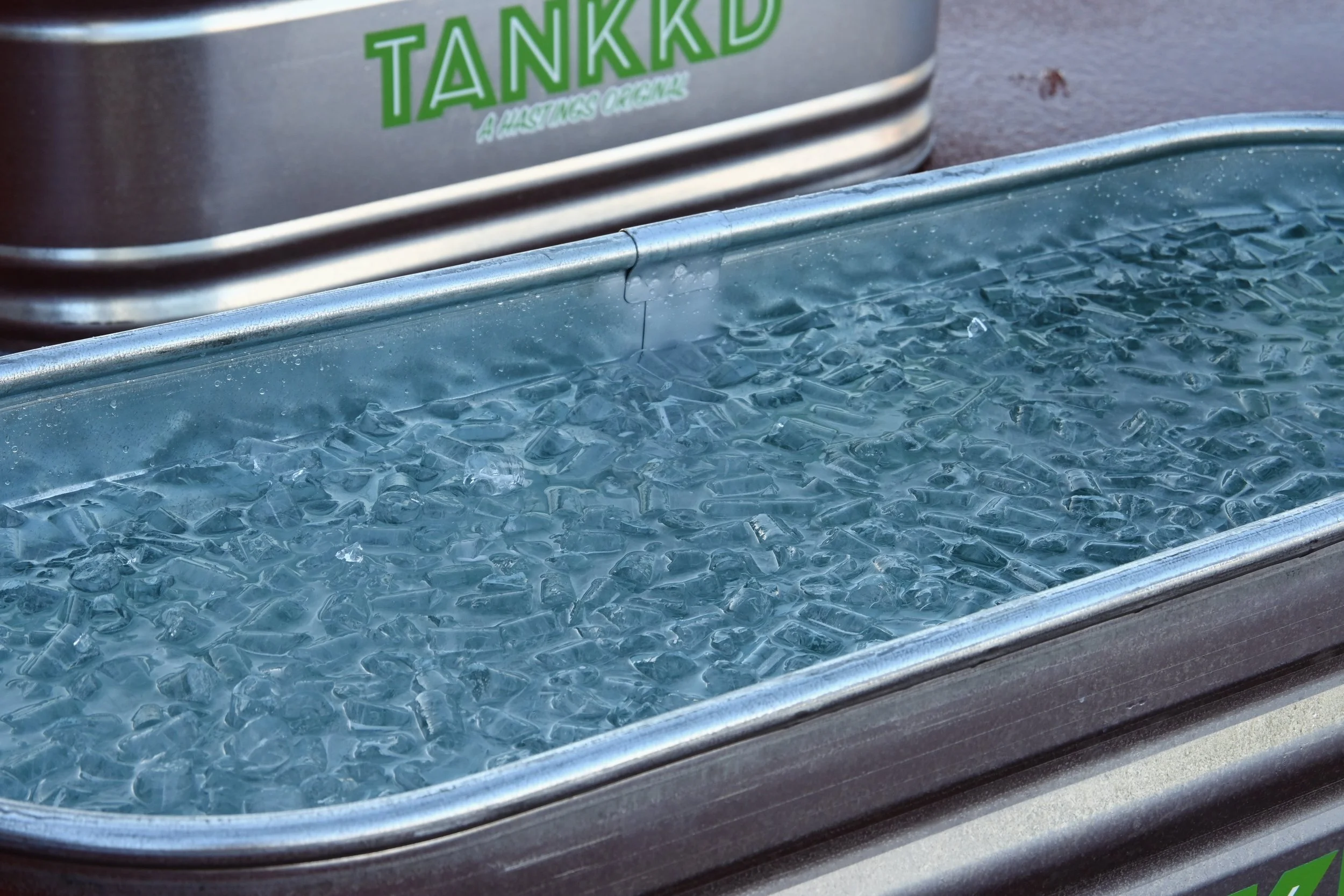 A metal trough filled with broken ice cubes, with a partially visible container in the background labeled 'TANKKD'