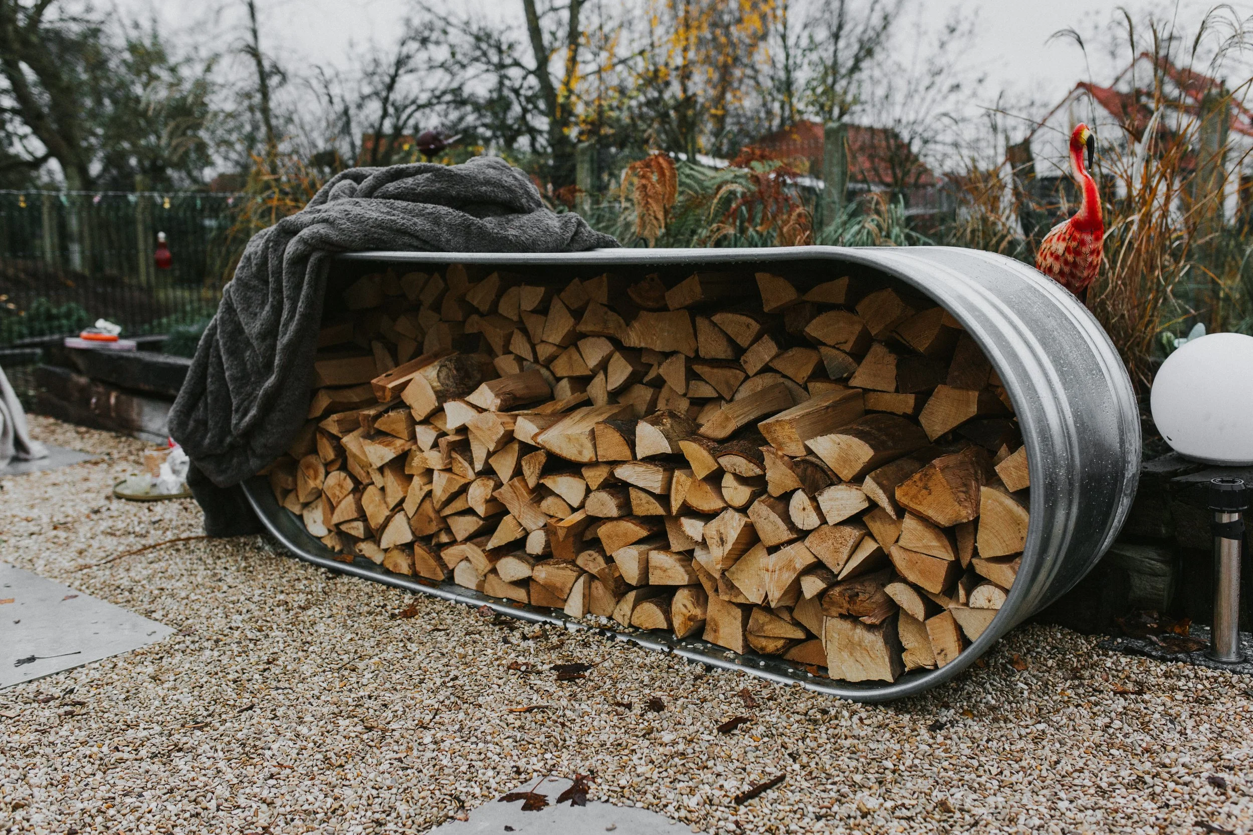 A Stock tank filled with cut firewood logs outside in a backyard.