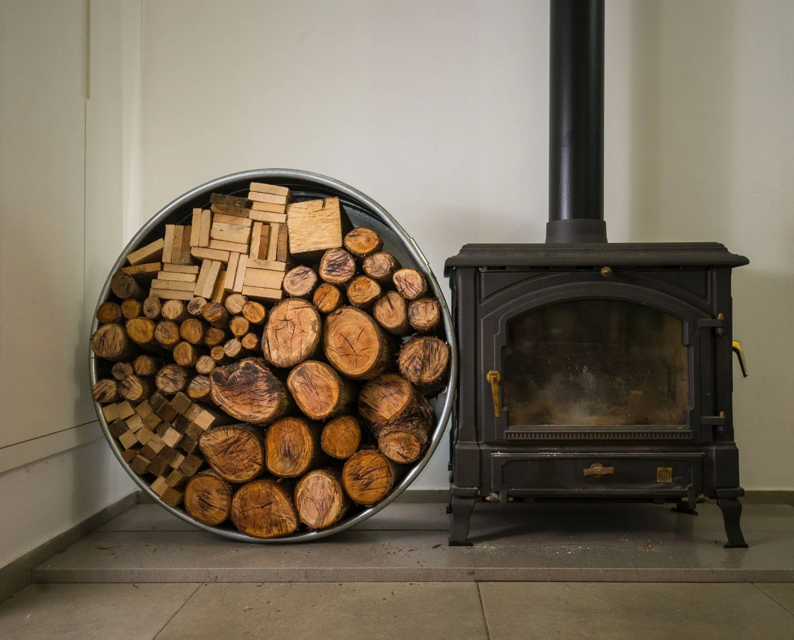 A neatly stacked pile of firewood next to a black wood stove in a room.