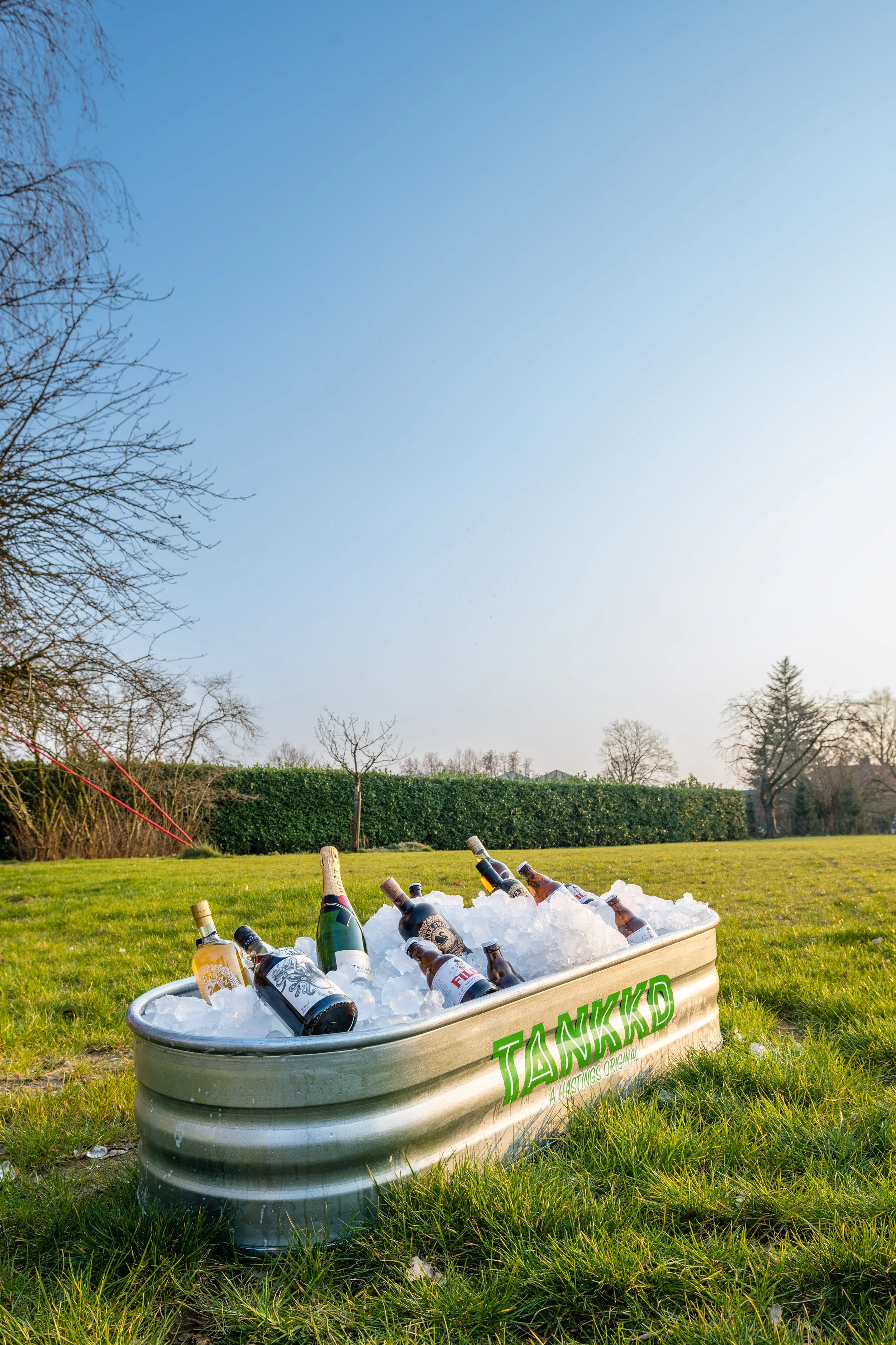 A Stock Tank filled with ice and bottles of alcoholic beverages in an outdoor grassy area on a sunny day.