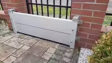 Flood barrier installed against a brick wall beside a black metal fence on a stone pavement.