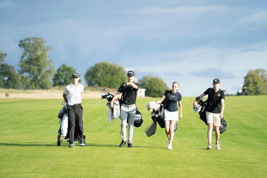 Fyra personer promenerar på en golfbana med golfklubbor under en klar himmel på Motala Golfklubb.