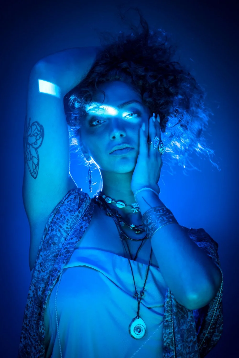 Woman in blue lighting with tattoos, jewelry, and curly hair