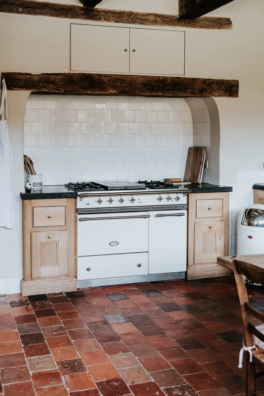Kitchen with a stove, wooden cabinets, white tiled backsplash, and a terracotta tiled floor.