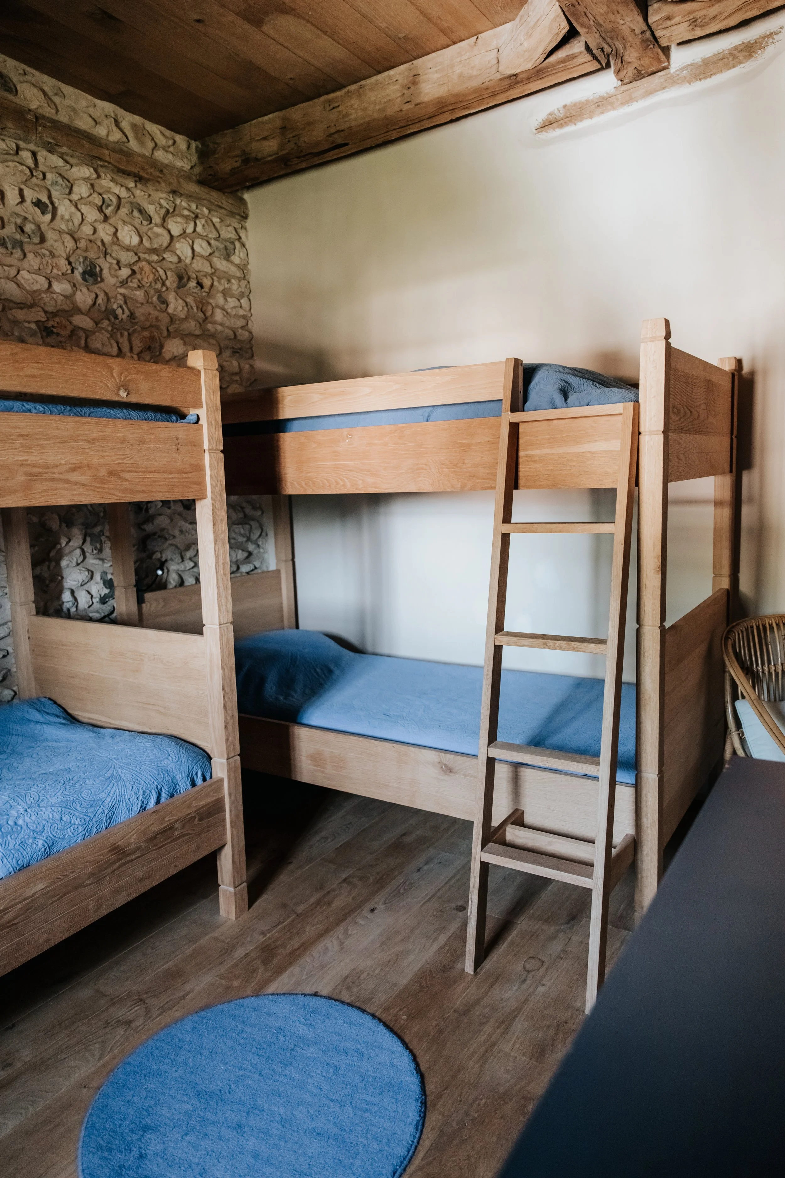Wooden bunk beds with blue bedding in a rustic room with stone wall and wooden ceiling.