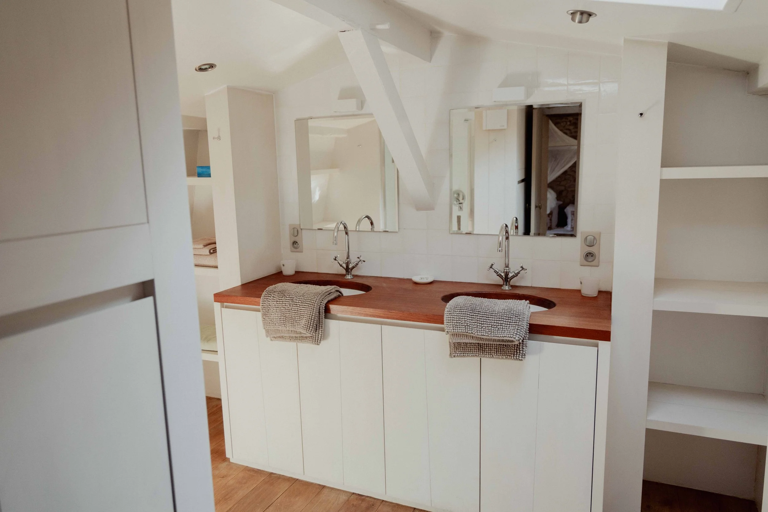 Een wit badkamermeubel met dubbelwasbakken, een houten countertop en twee spiegels boven de wastafels.