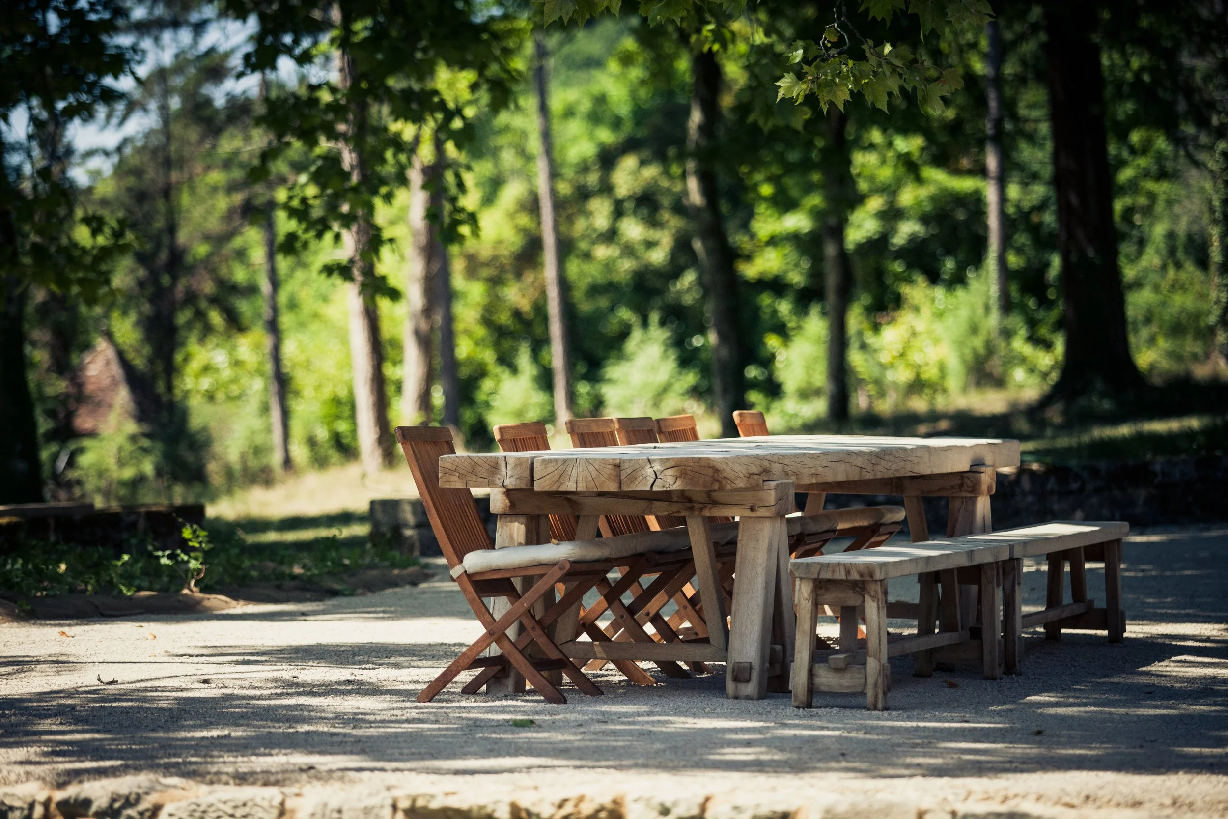 Een houten tafel met bijbehorende stoelen en bank in een bosrijke omgeving met veel groen en bomen.