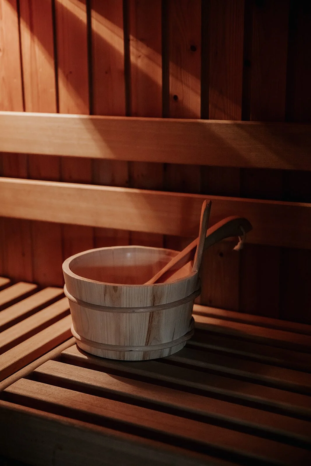 Interior of a wooden sauna with a wooden bucket and ladle on a slatted bench.