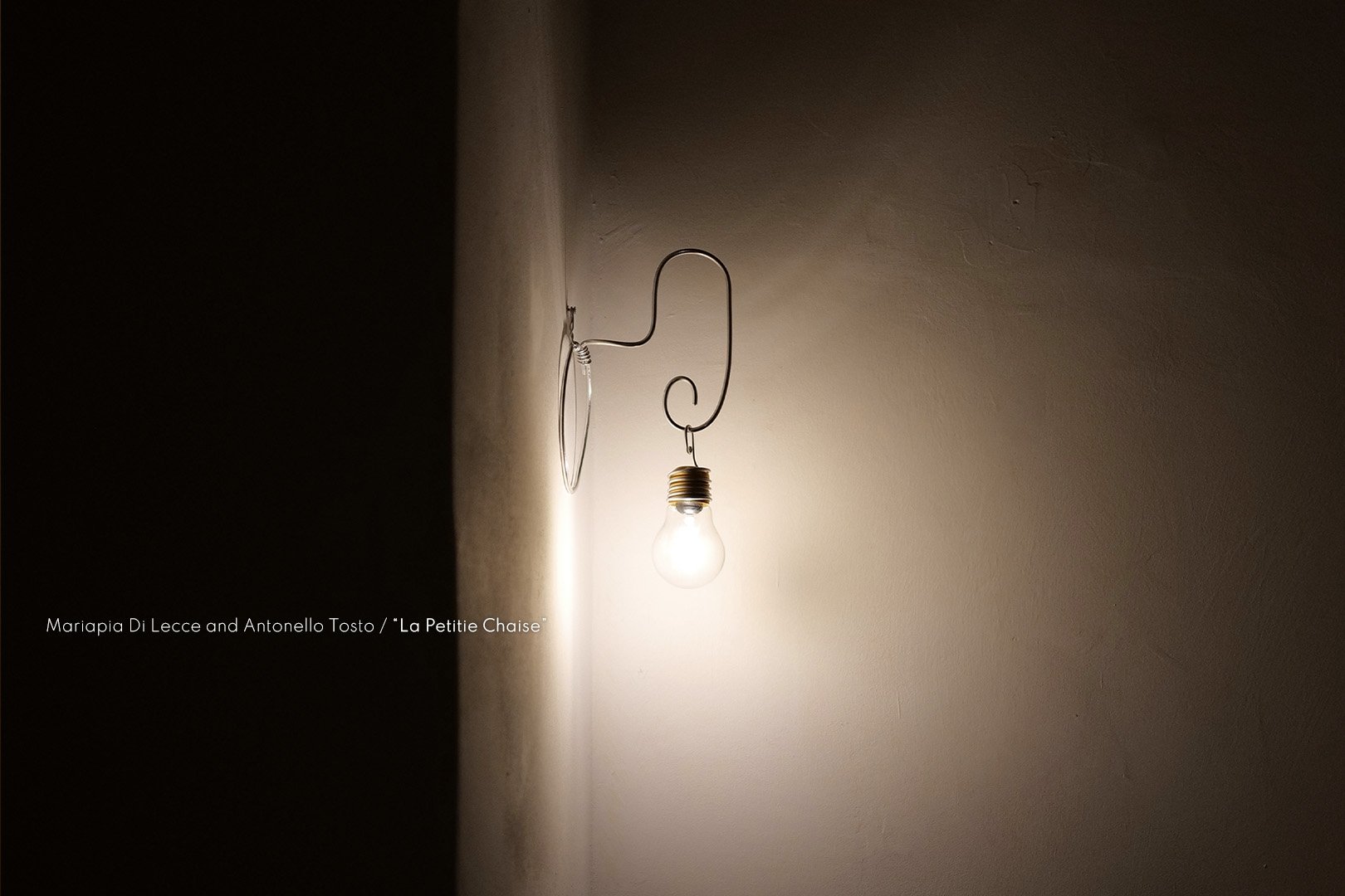 A wall with a light bulb hanging from a wire, illuminating the surrounding area, with part of the wall in shadow.
