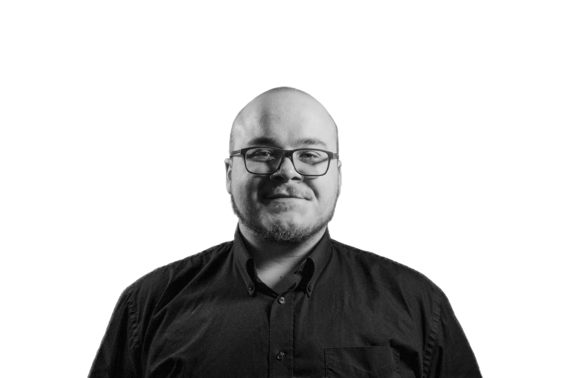 Black and white portrait of a man with glasses, short hair, and a beard, wearing a dark button-up shirt against a white background.