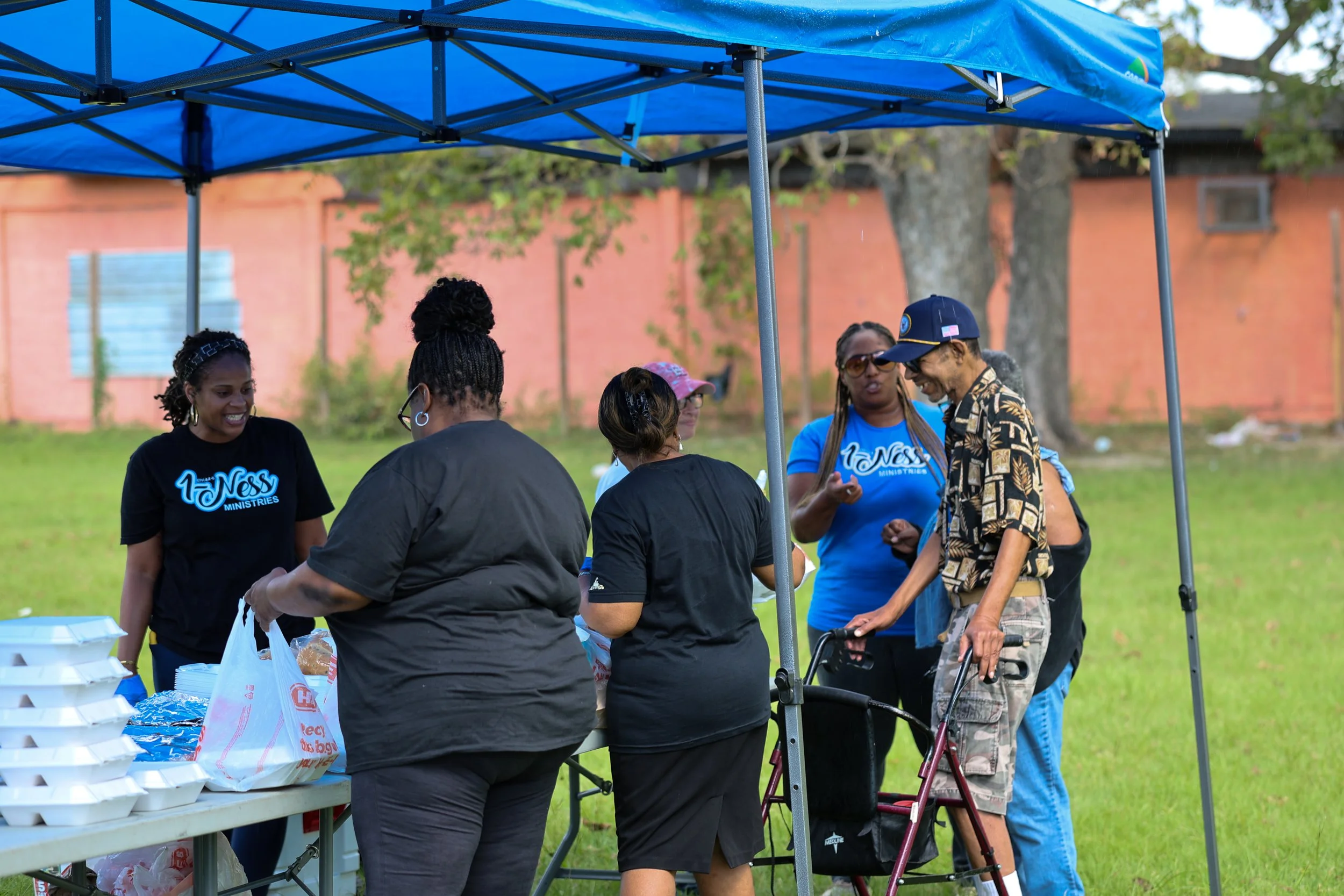 People distributing food outdoors at a community event, with tables set up and trays of food visible.