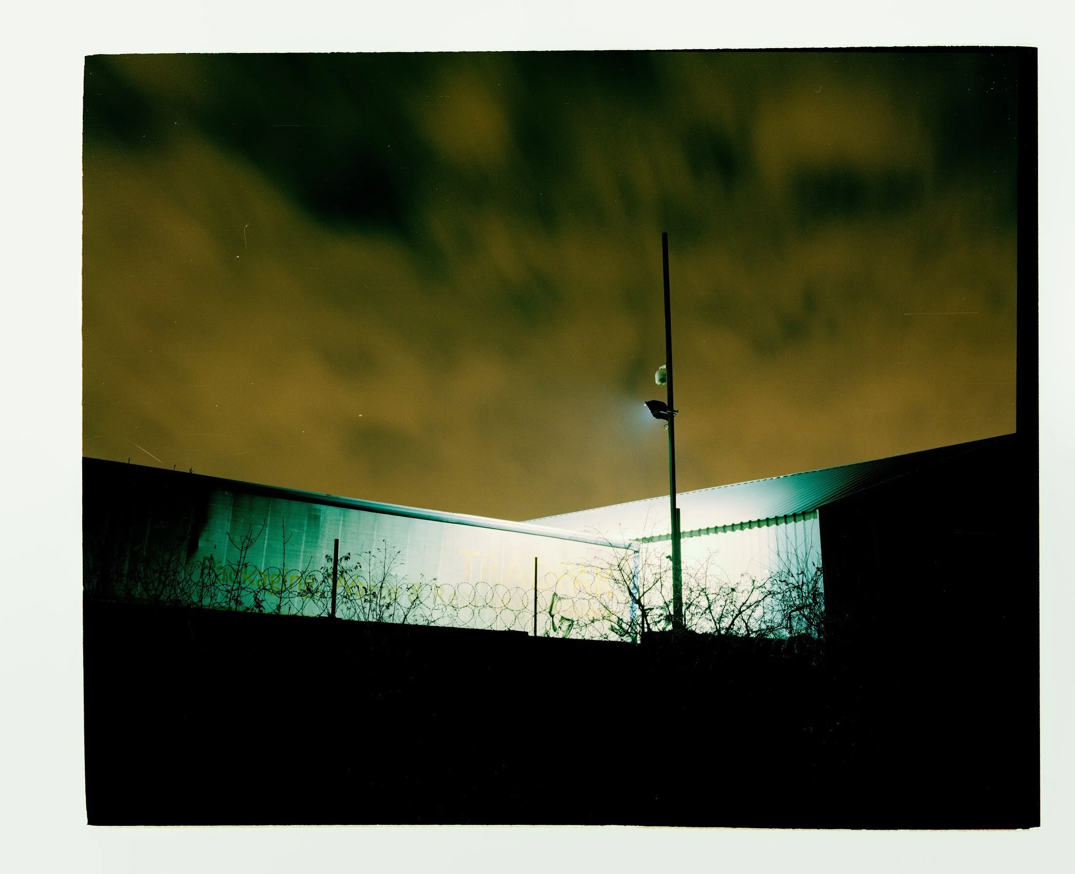 Night sky with green aurora borealis, stars, and a tall streetlight illuminating a dark area below.