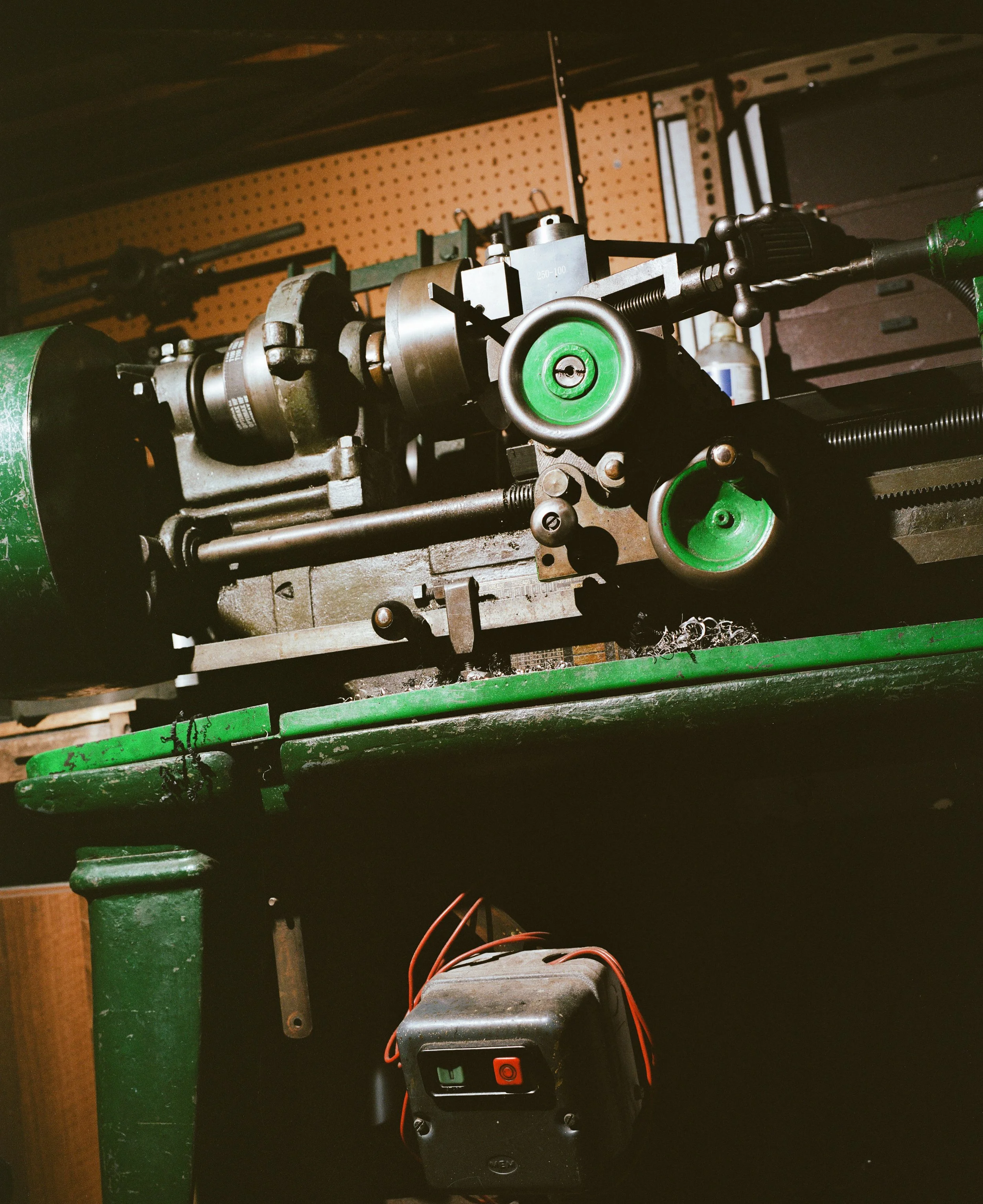 Close-up of a metal lathe machine with green handles, mounted on a green workbench in a workshop.