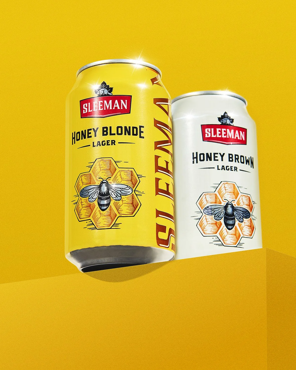 Two branded honey blonde ale cans prominently displayed on a bold solid yellow background, clean and vibrant commercial product packaging shot