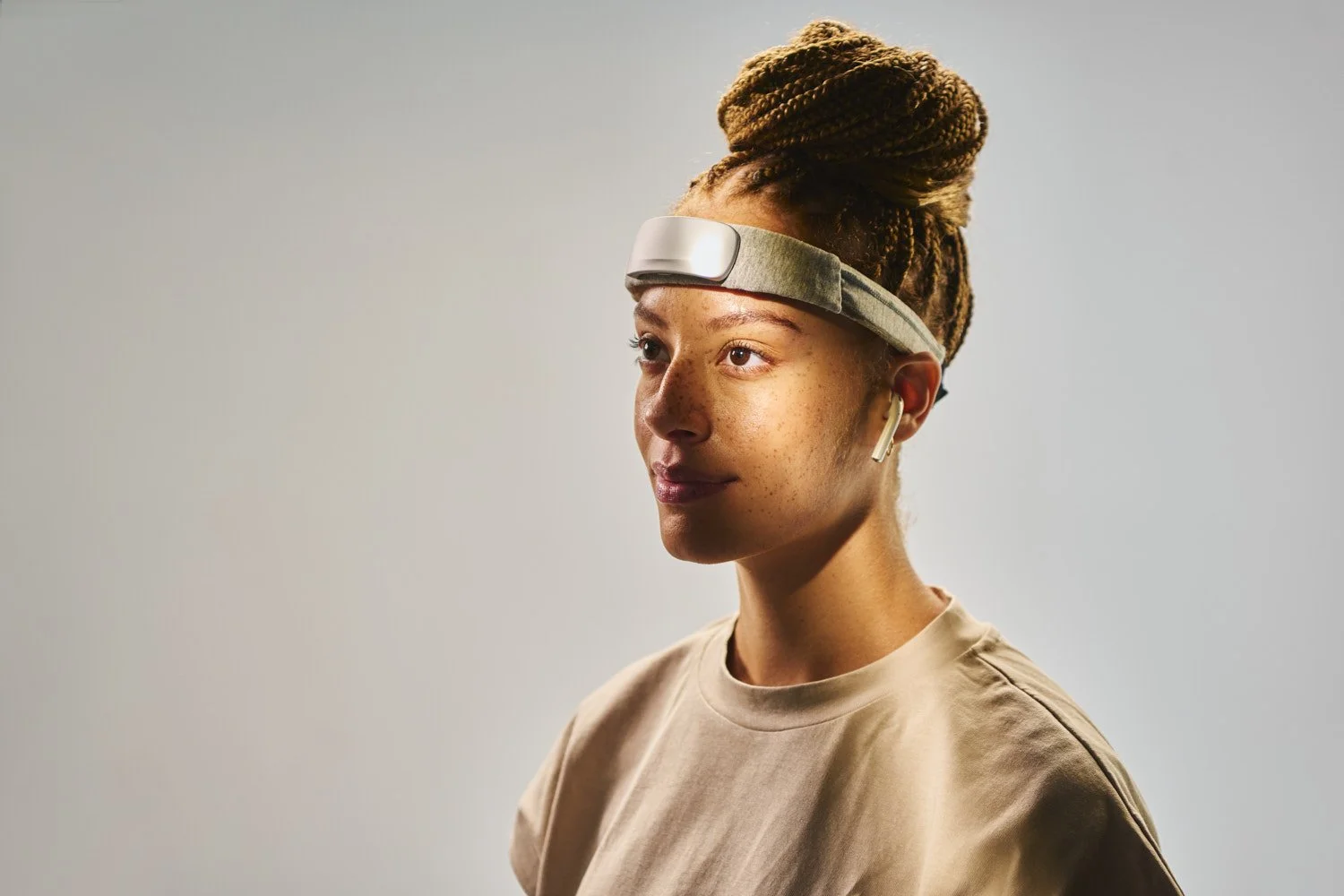 Side profile of a woman with hair up wearing a slim tech headband wearable, shot on a warm neutral background with soft lifestyle portrait lighting