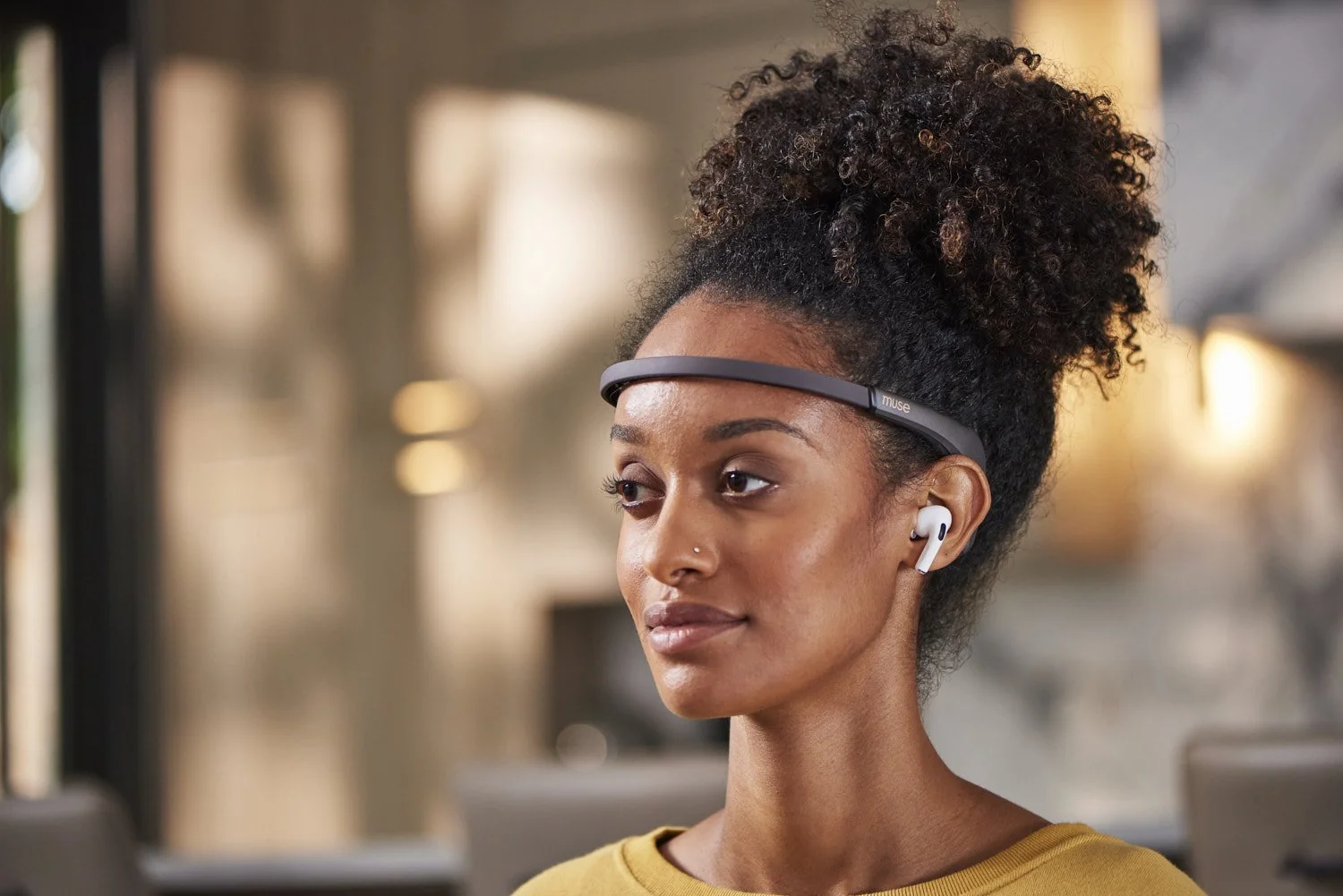 Young Black woman with natural hair wearing wireless earbuds and a tech headband wearable, lifestyle portrait in a warmly lit contemporary interior with golden tones
