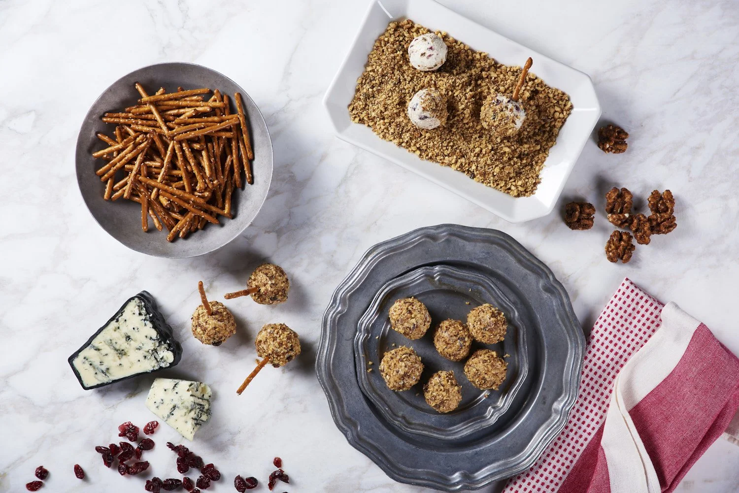 Overhead flat lay of assorted snacks including nuts, pretzels, cheese, crackers, and dried fruit arranged loosely across a white marble surface