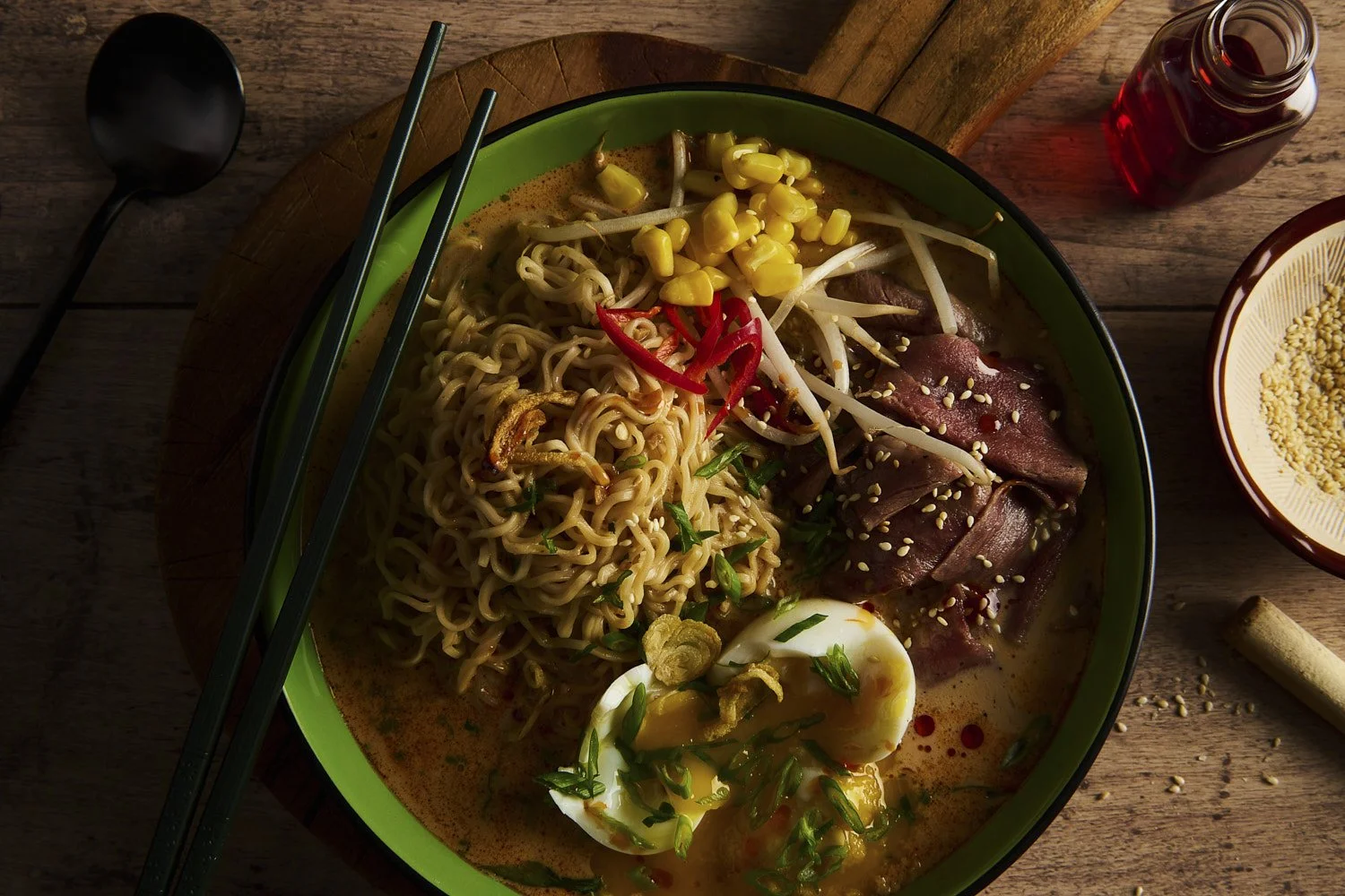 Dark and moody overhead shot of noodle stir-fry with tender braised meat, vegetables, and sauce in a deep cast iron pan on a textured surface
