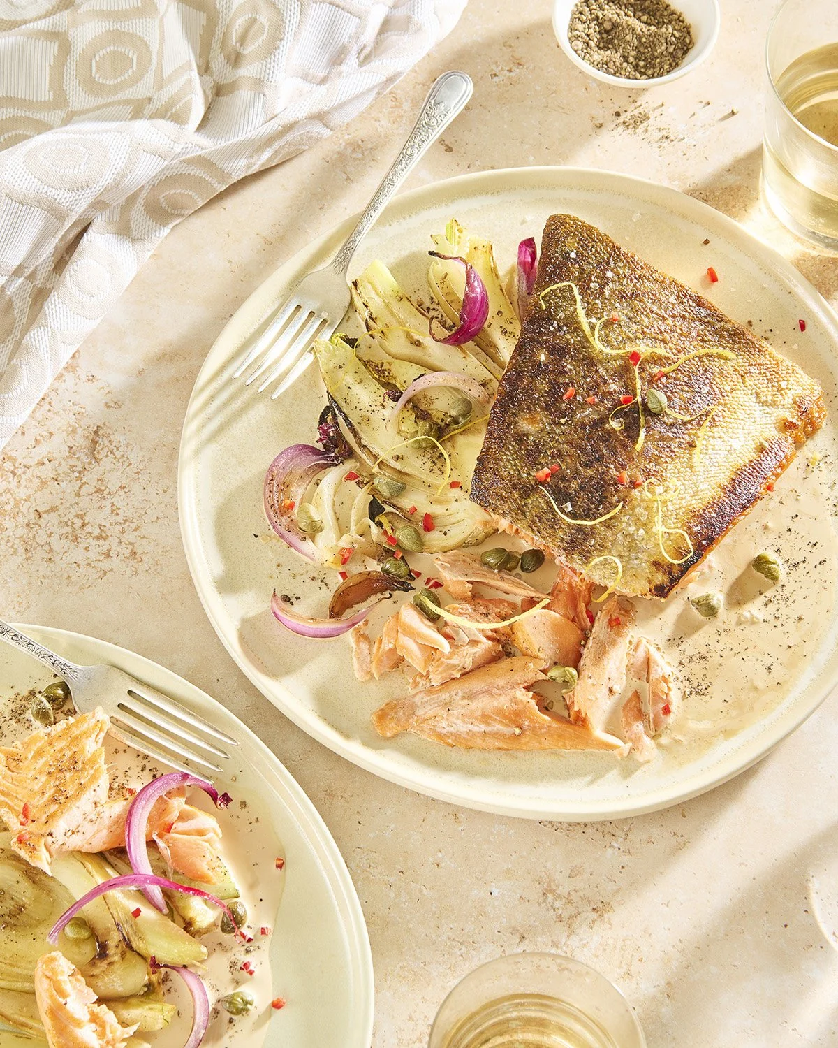 Top-down view of a delicate white fish fillet in creamy sauce with artichoke slices and capers, served in a shallow bowl on a light surface
