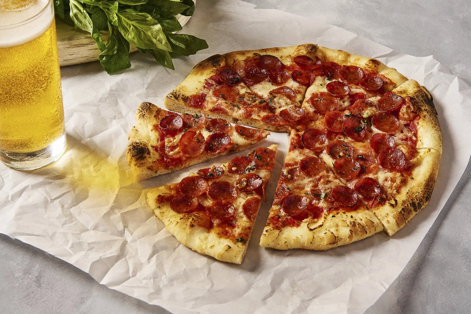 Loaded pepperoni and vegetable pizza on crinkled parchment paper, served alongside a glass of fresh orange juice on a warm wood and linen surface