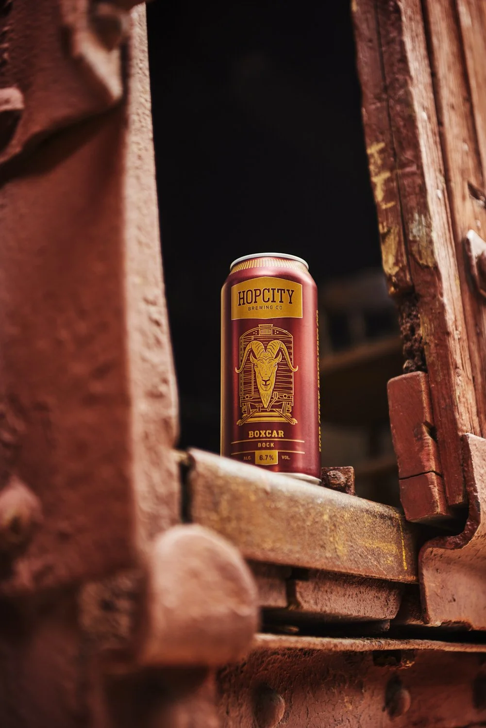 Single branded energy or craft beverage can tucked into a rustic weathered wooden window frame, moody lifestyle product shot with warm ambient light
